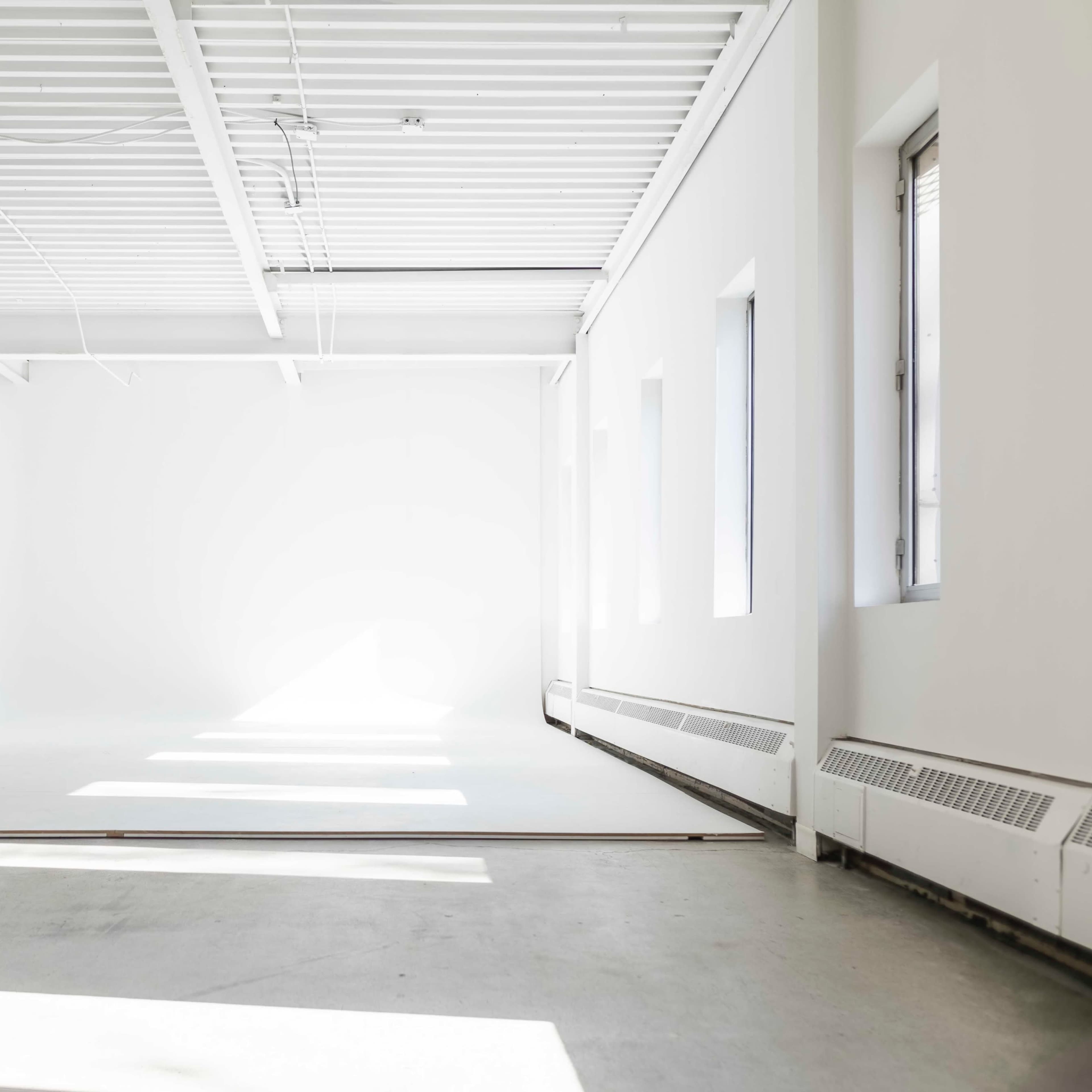 A spacious, well-lit studio features a large white backdrop and concrete floor.