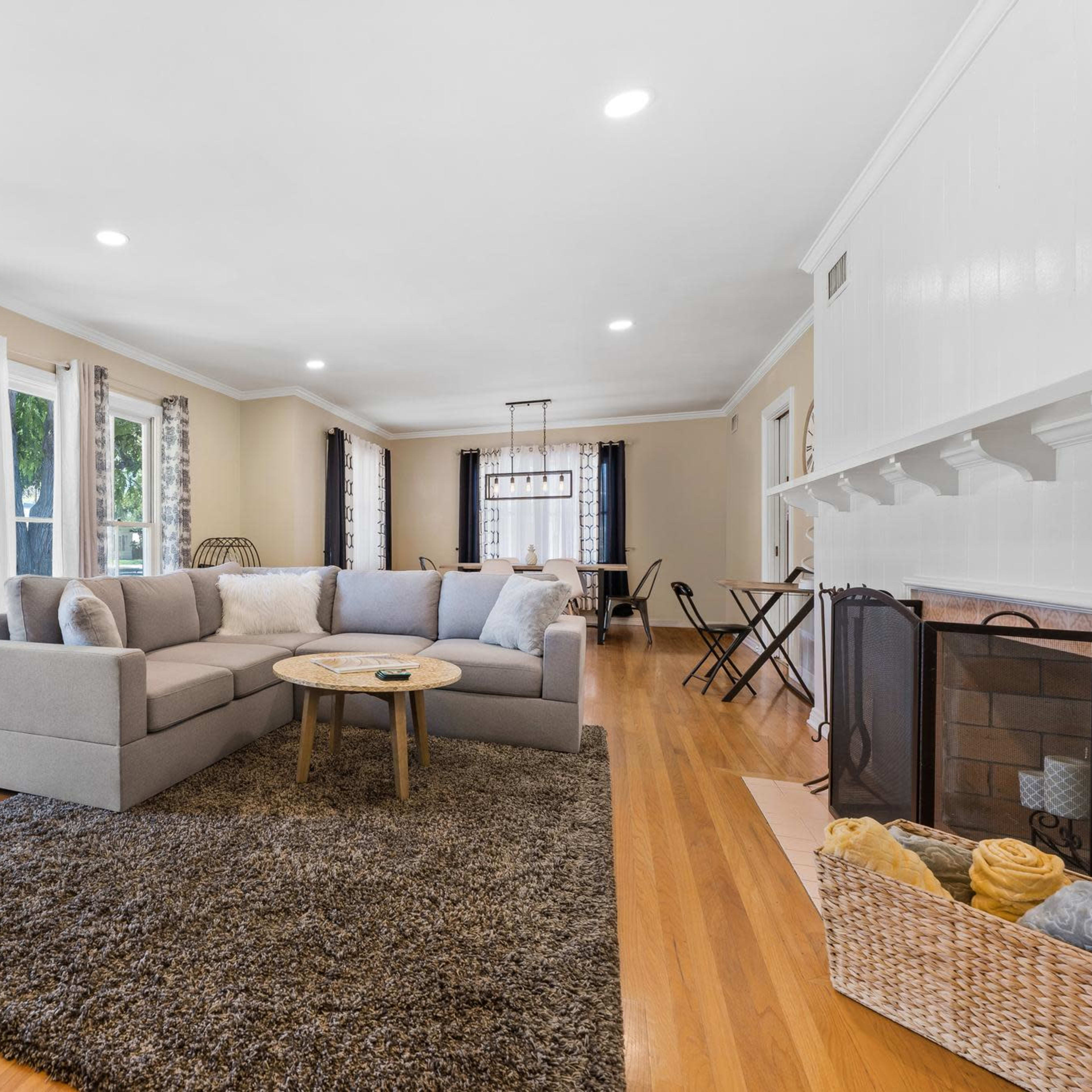 A spacious living room features a large sectional sofa, a round table, and large windows that let in ample natural light.