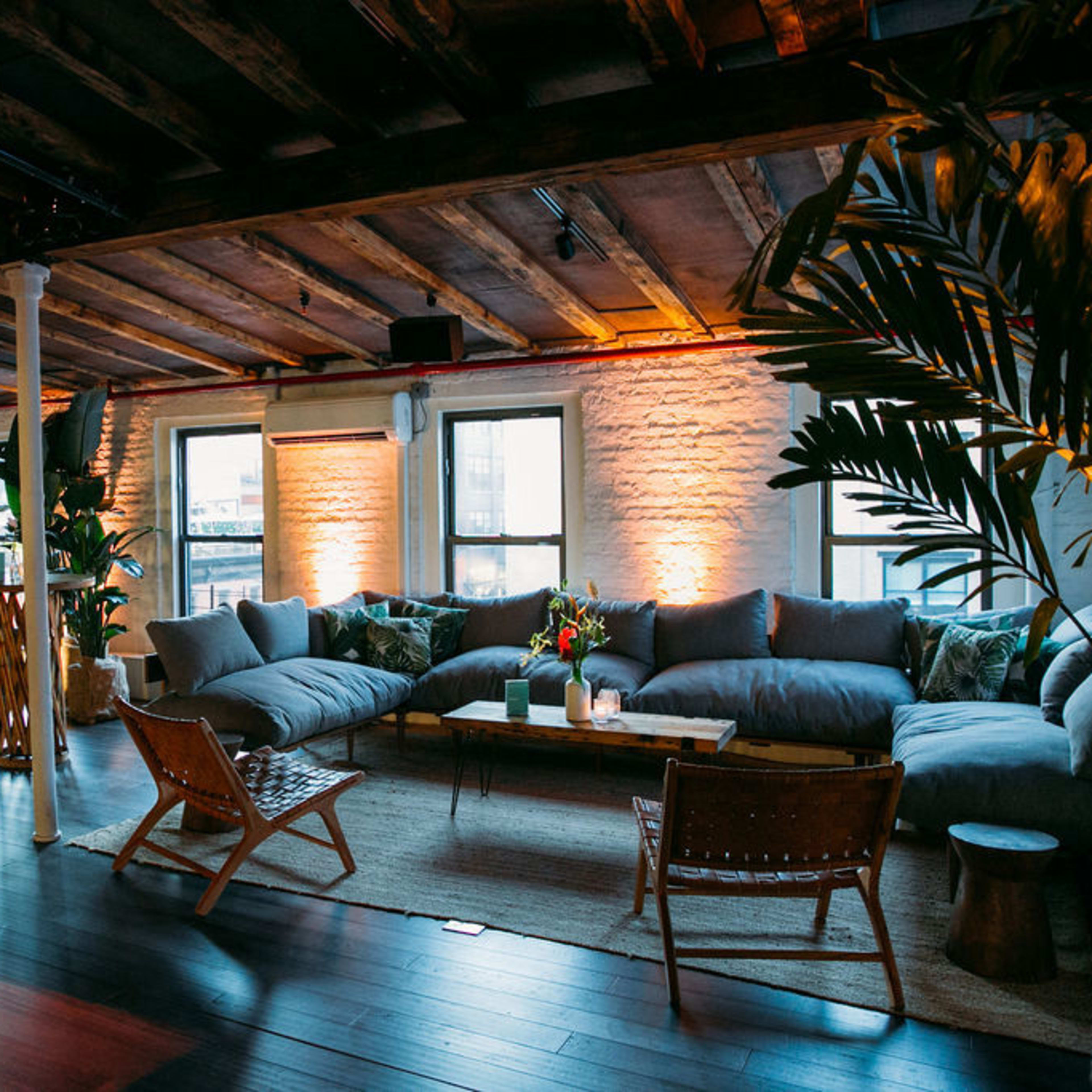 A spacious lounge area with comfortable seating, wooden beams, and plants, illuminated by soft lighting.