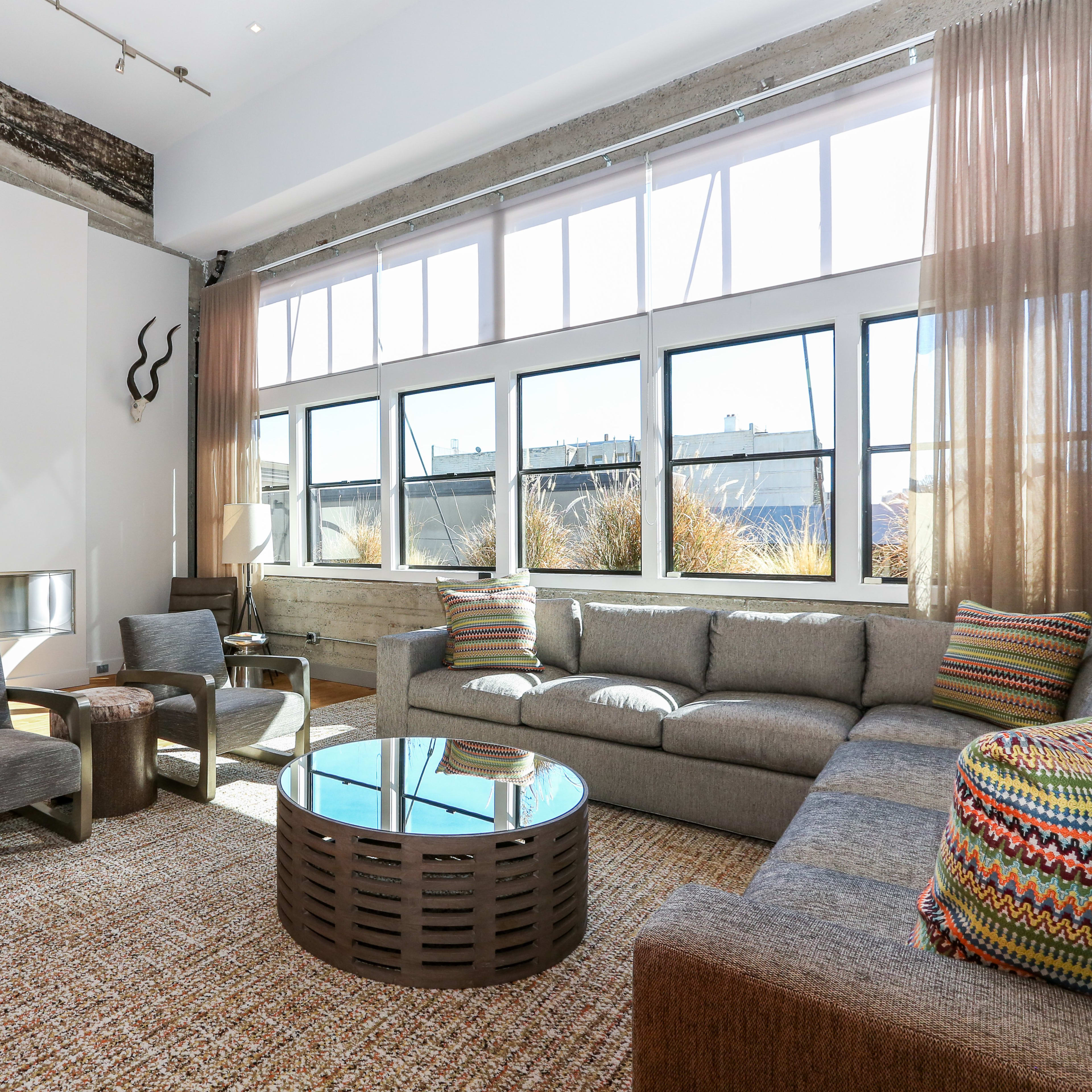 A modern living room with large windows, a gray sofa, a round coffee table, and decorative elements like animal horns on the walls.