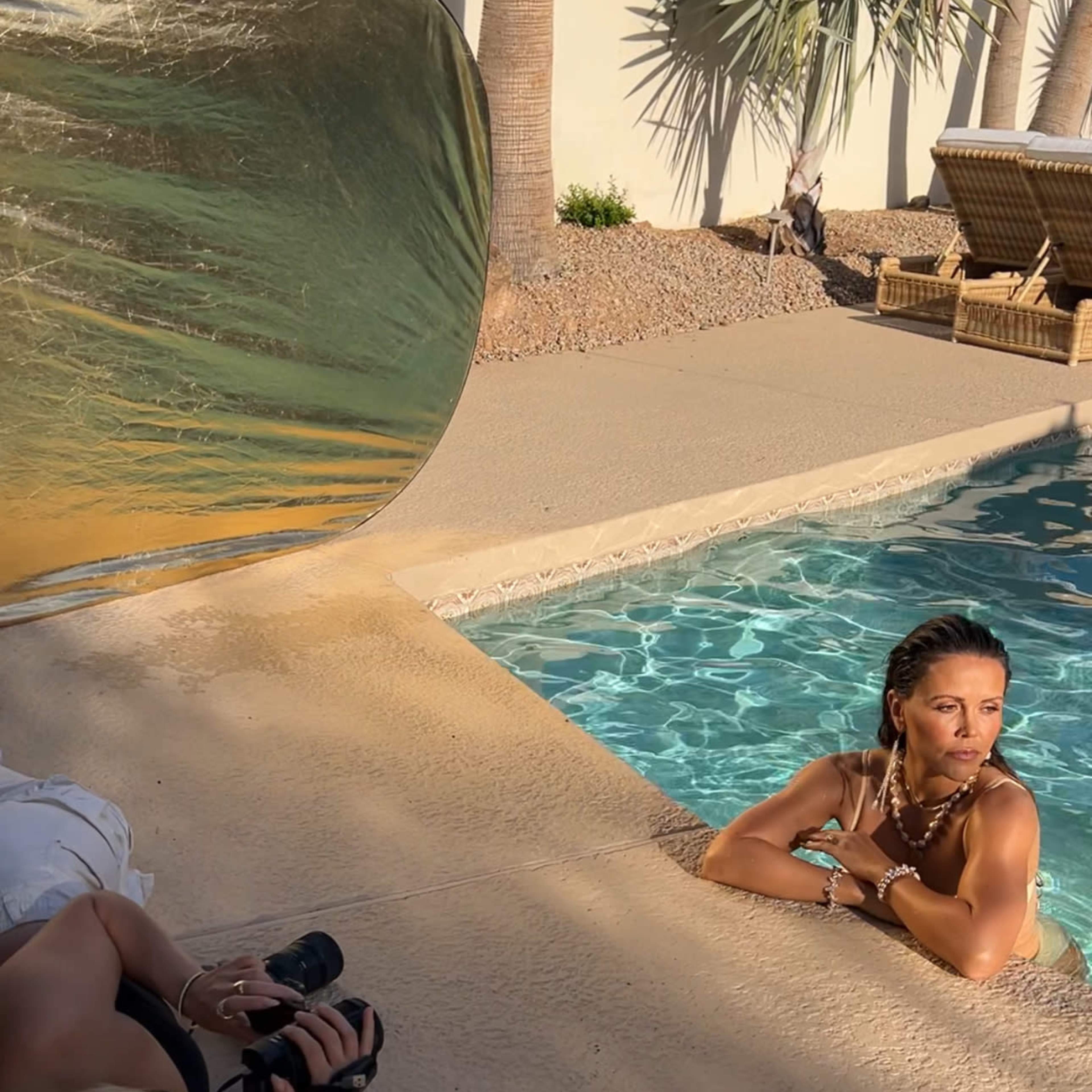 A model poses by a swimming pool while a photographer captures the scene from the edge of the pool.