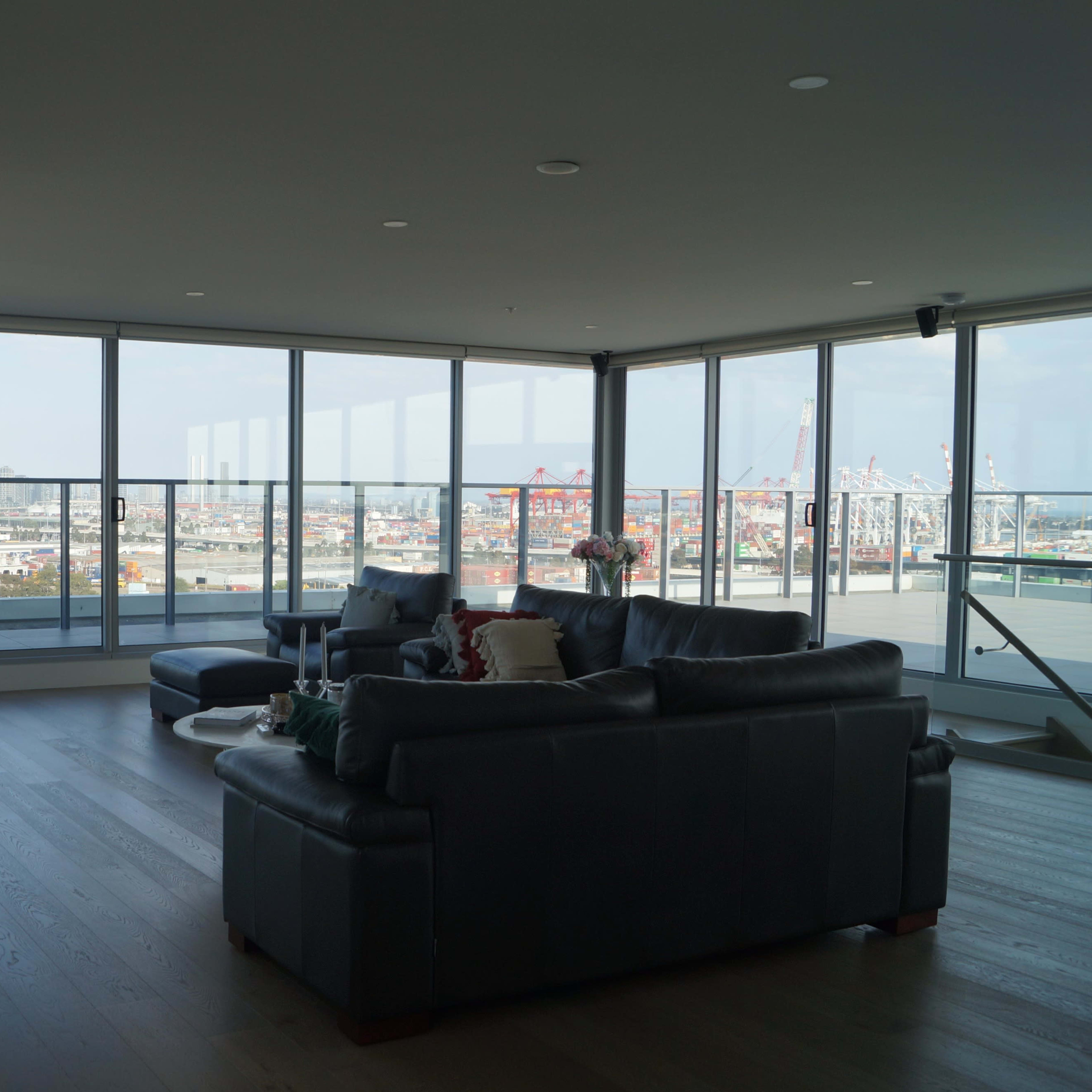 A modern living room with large windows offering a view of a city skyline and port.