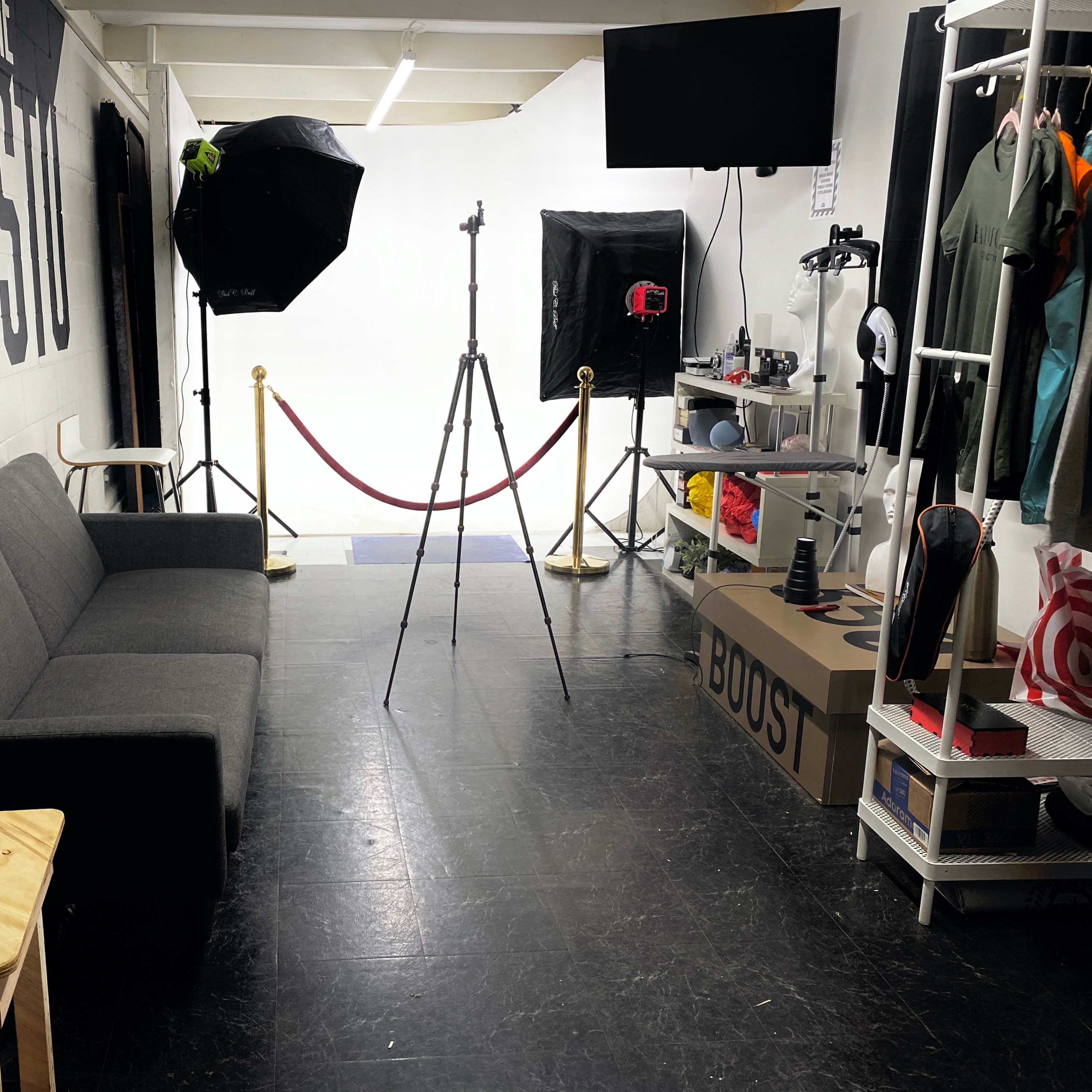 A photo studio featuring a gray sofa, a wooden table, photography equipment, and a backdrop.
