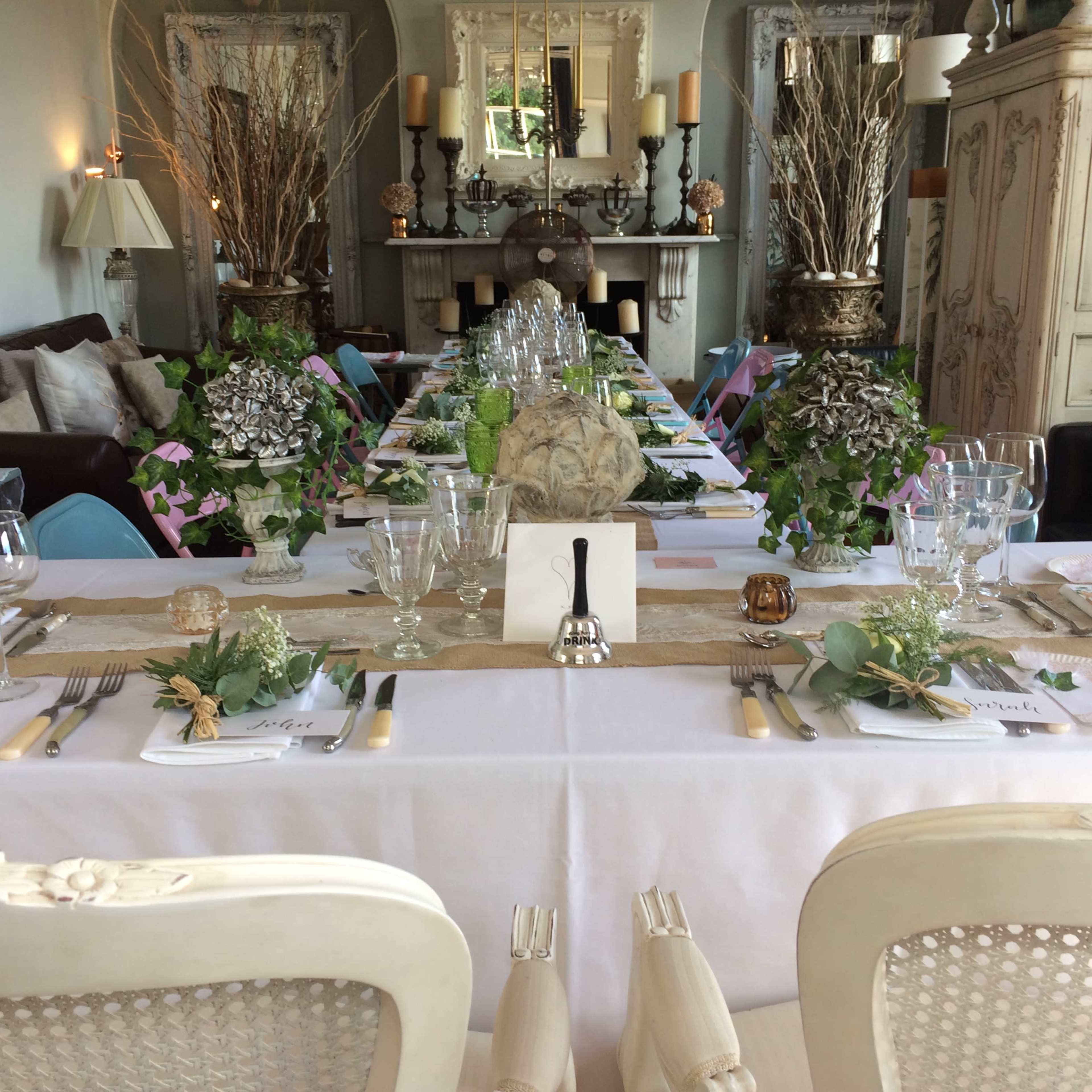 A long dining table is elegantly set with glassware, cutlery, and floral centerpieces in a well-decorated room.