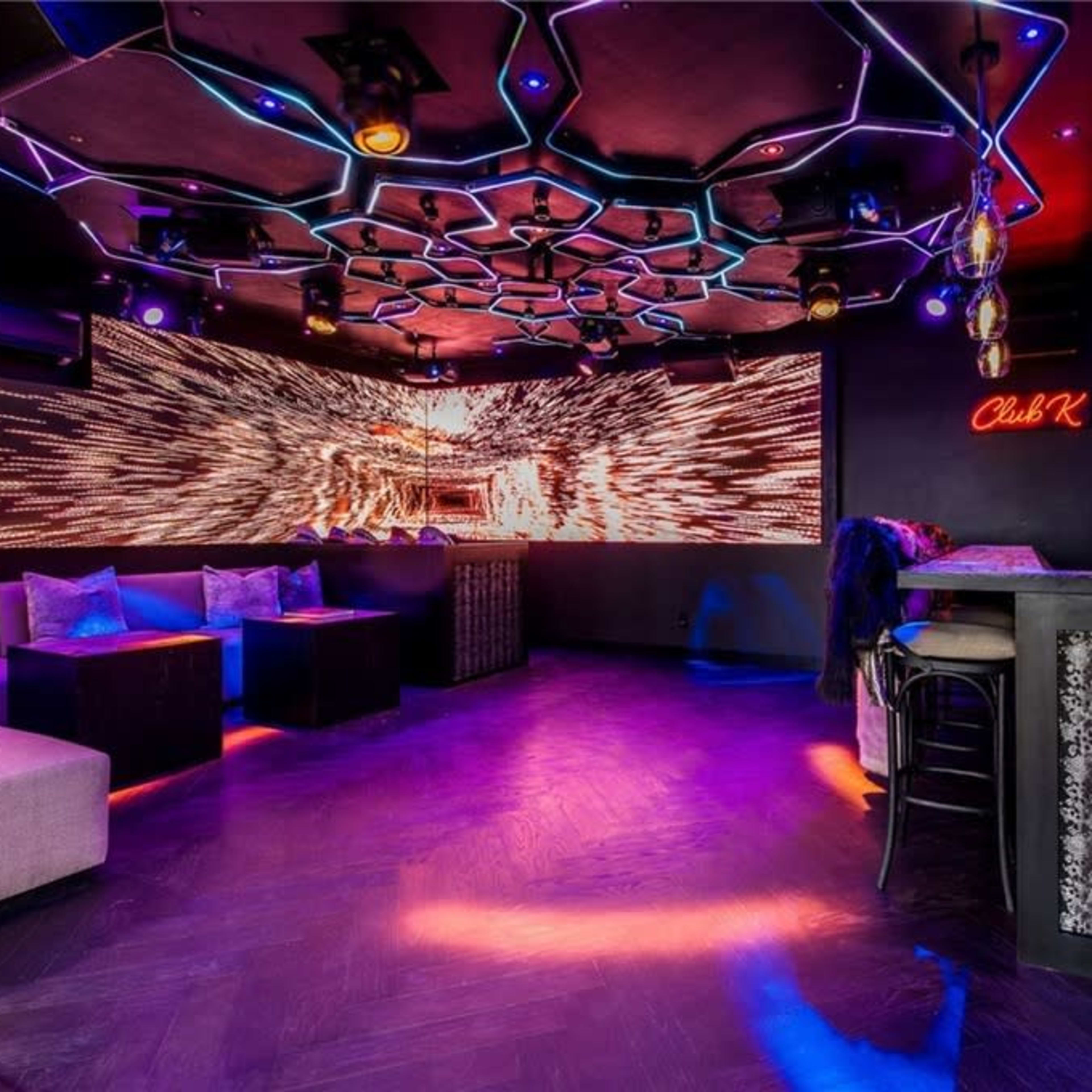 A modern lounge area with hexagonal ceiling designs and vibrant lights, featuring a bar counter and seating.