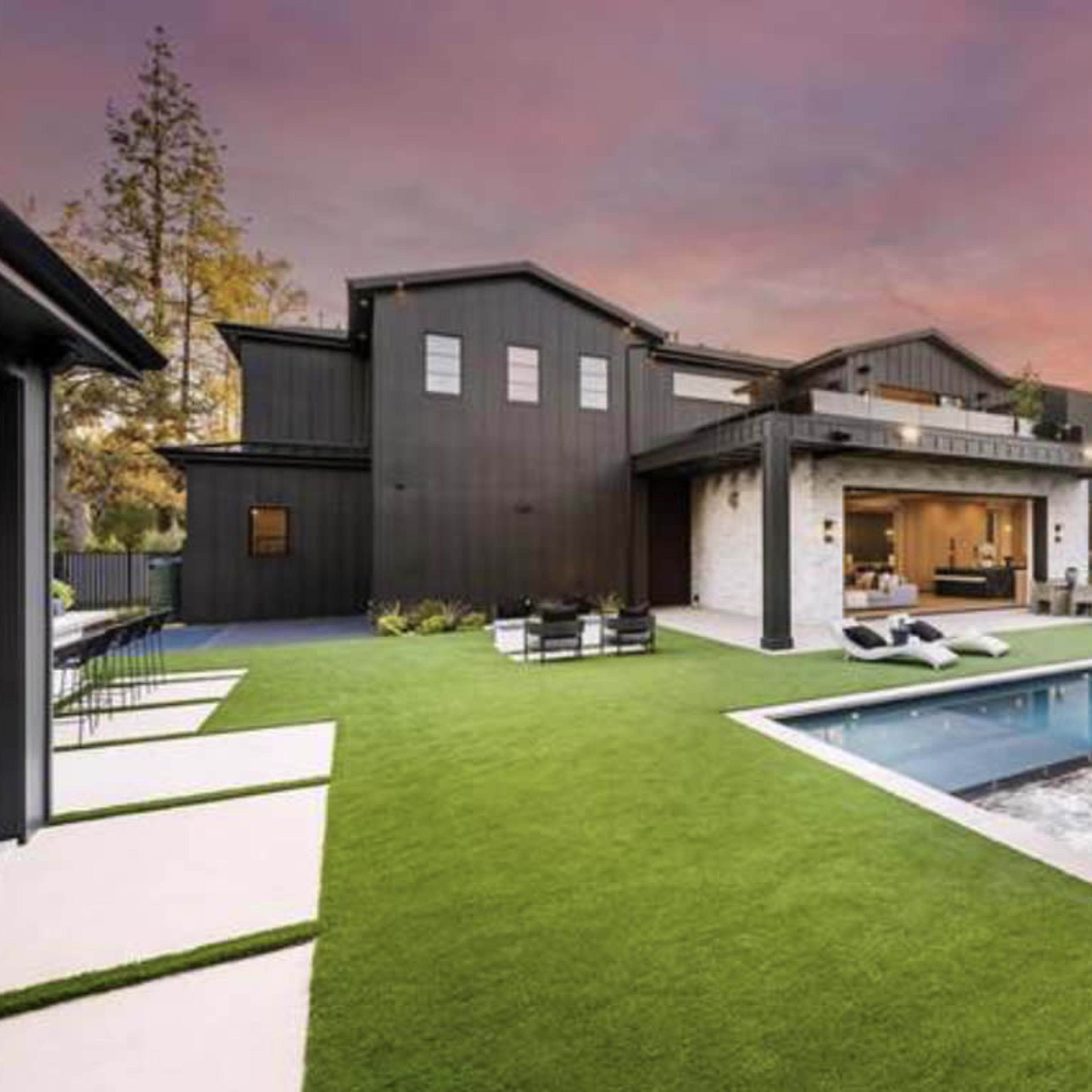 A modern house with a sleek design, a swimming pool, and a landscaped yard featuring artificial grass and outdoor seating areas.