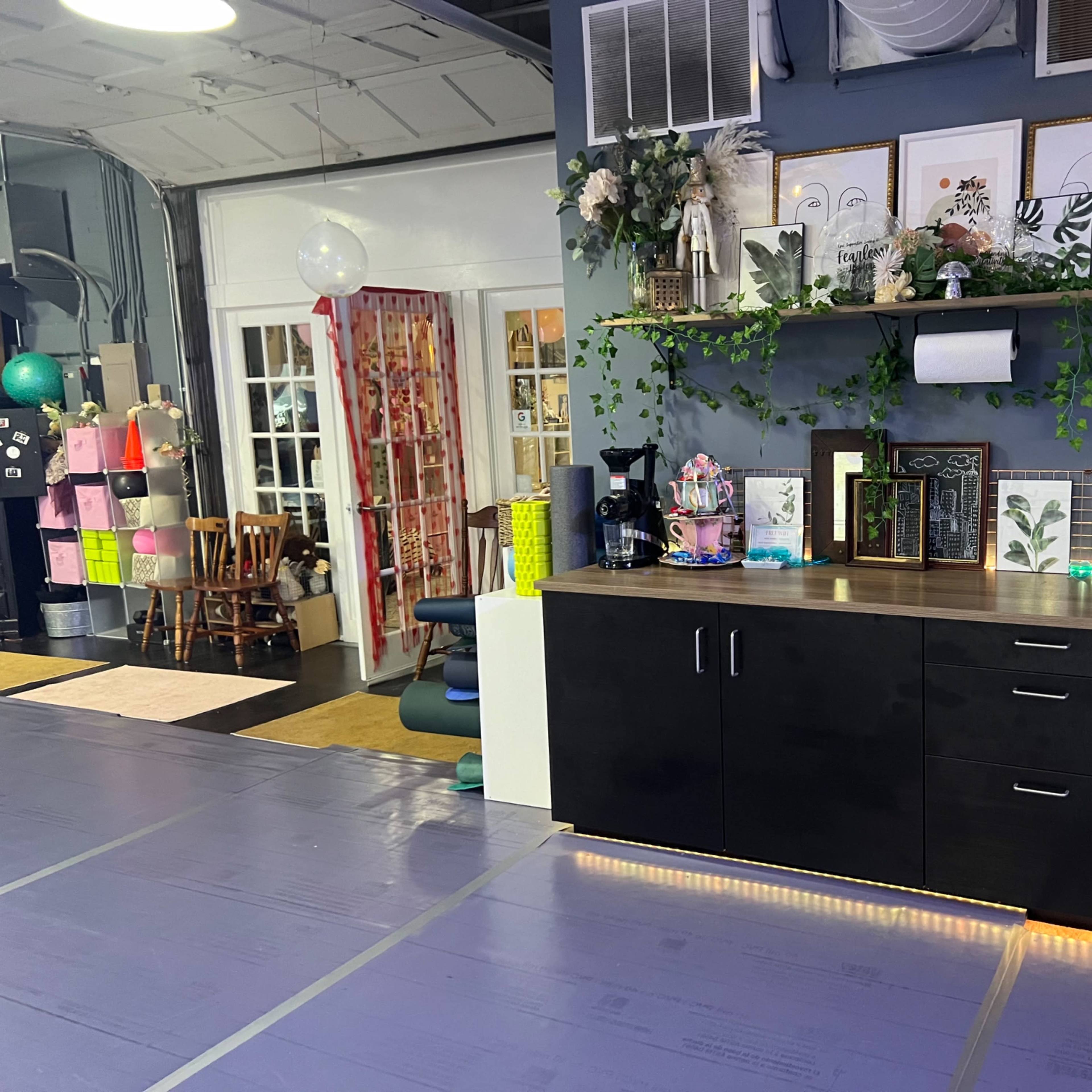 A room with a countertop featuring various decorative items, plants, and a sink, alongside a doorway that leads to another area with colorful decor.