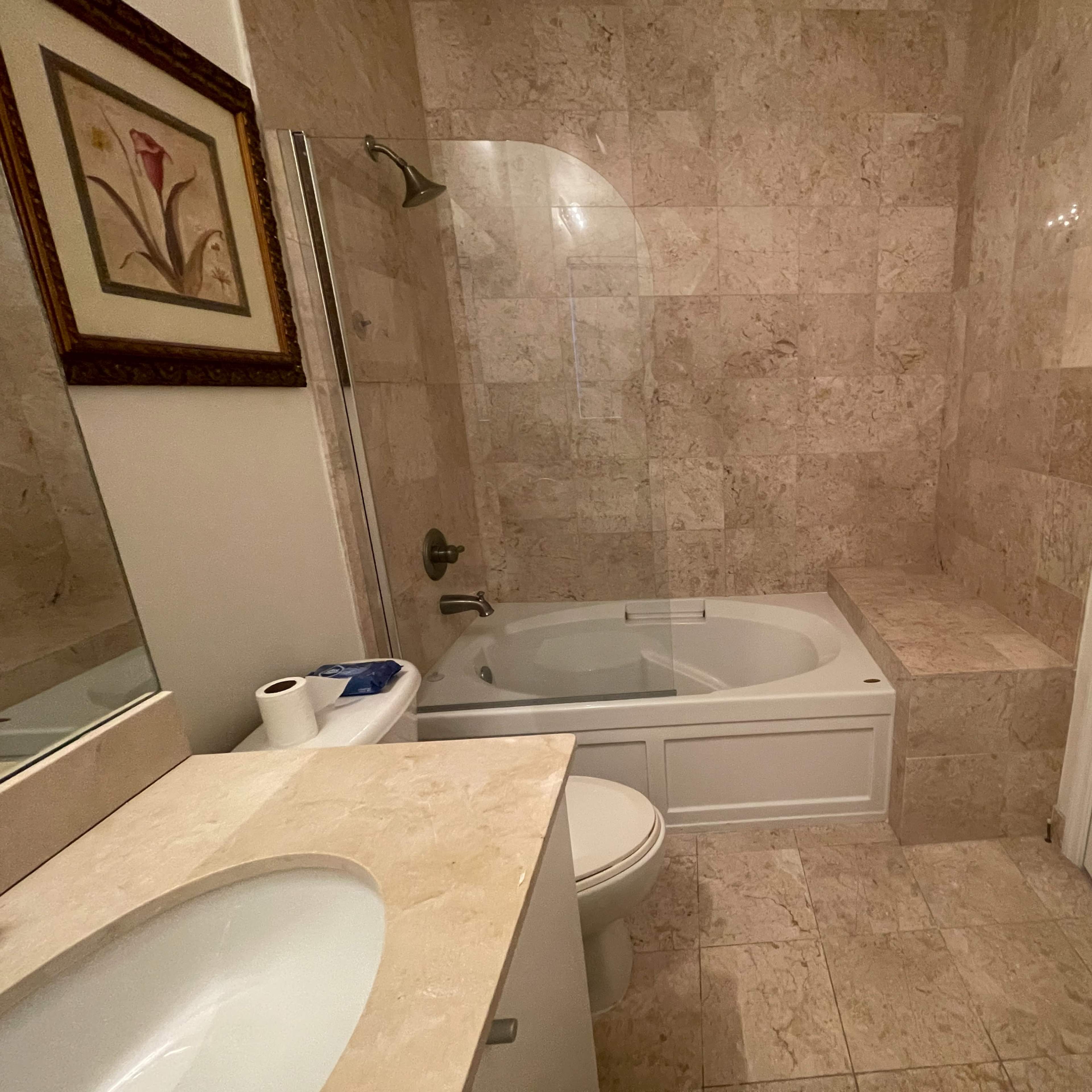 A bathroom featuring a bathtub, a toilet, a sink with a countertop, and marble wall and floor tiles.