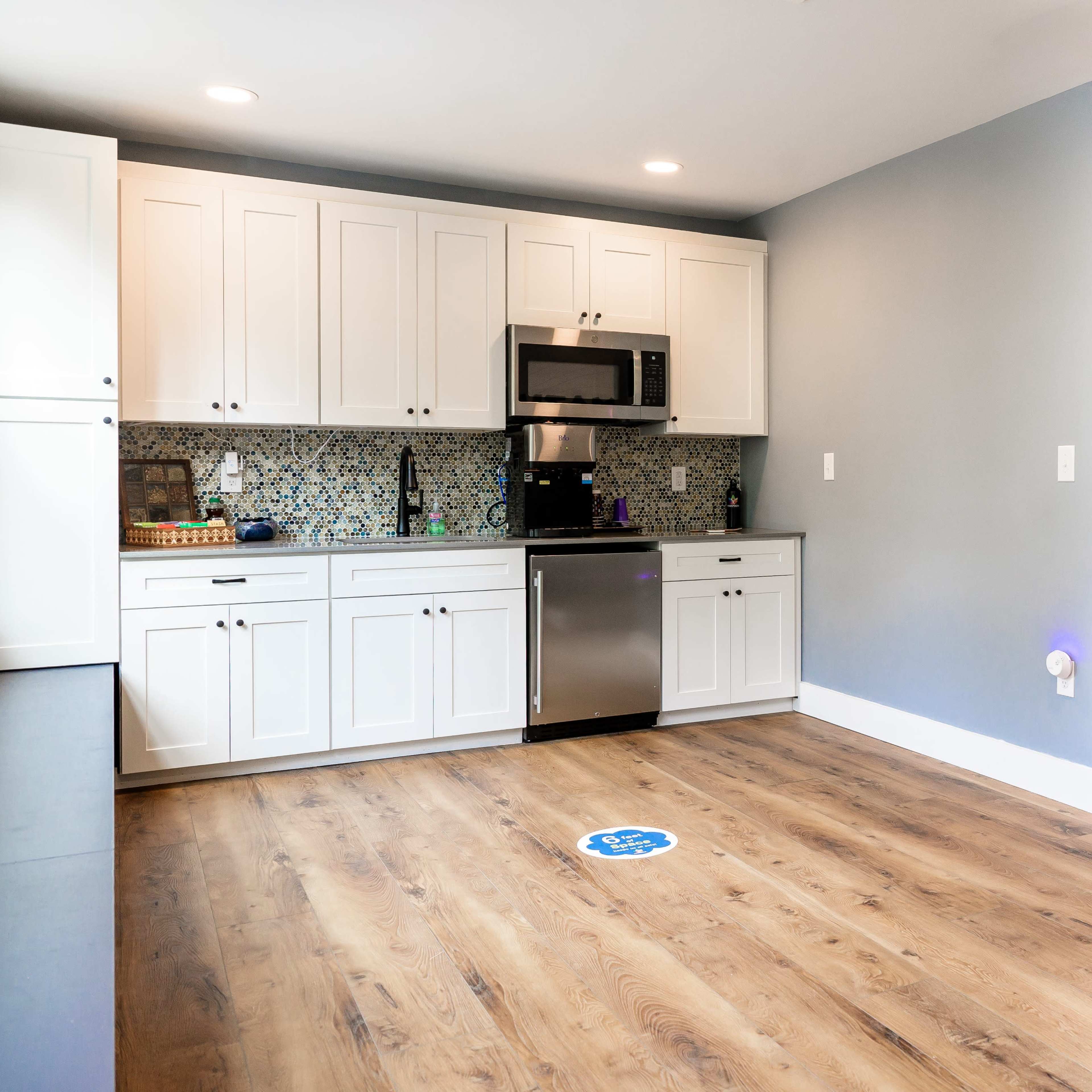 A modern kitchen features white cabinets, stainless steel appliances, and a wooden floor with a whiteboard on the wall.
