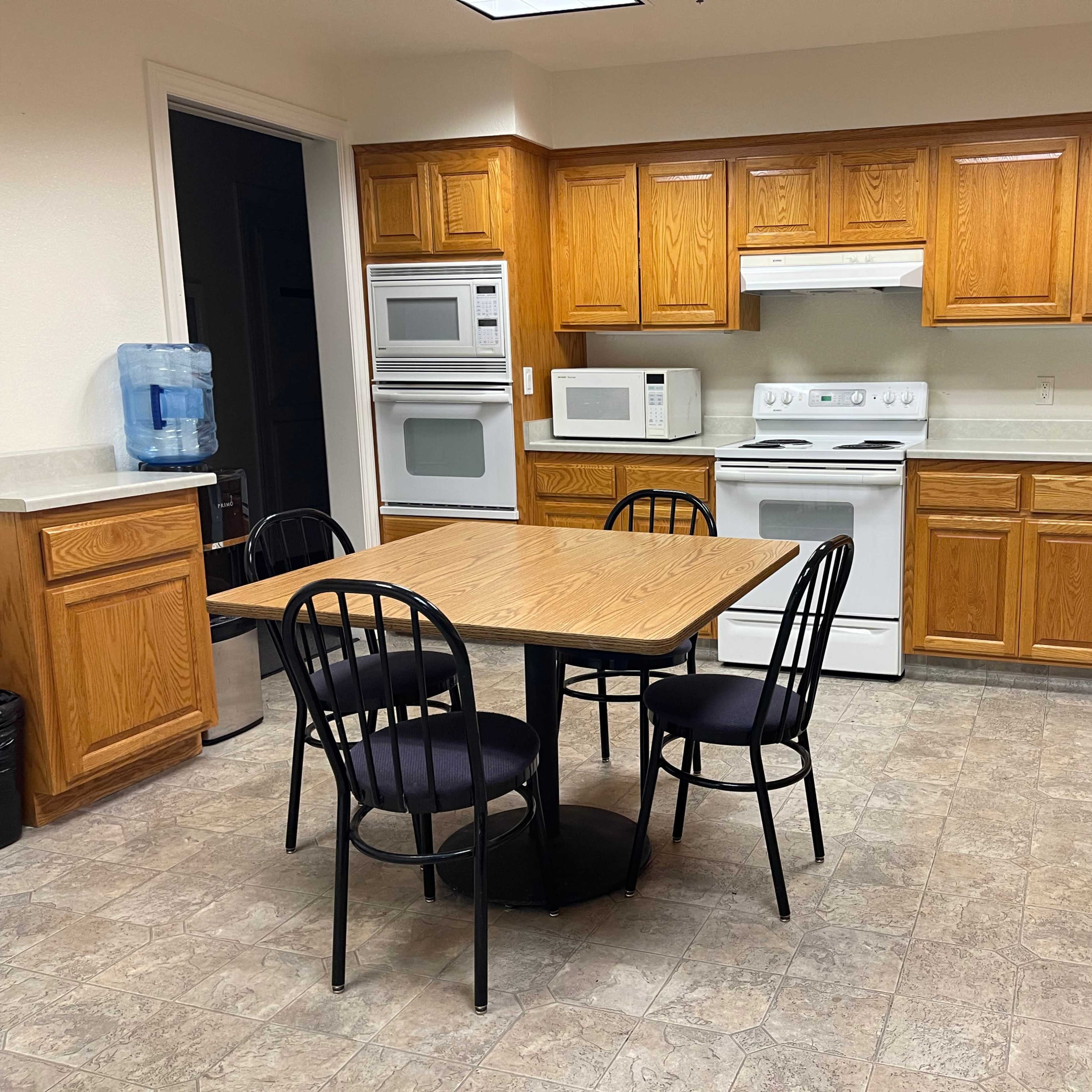 A kitchen with wooden cabinets, a table and four chairs, and various appliances including a microwave and a refrigerator.