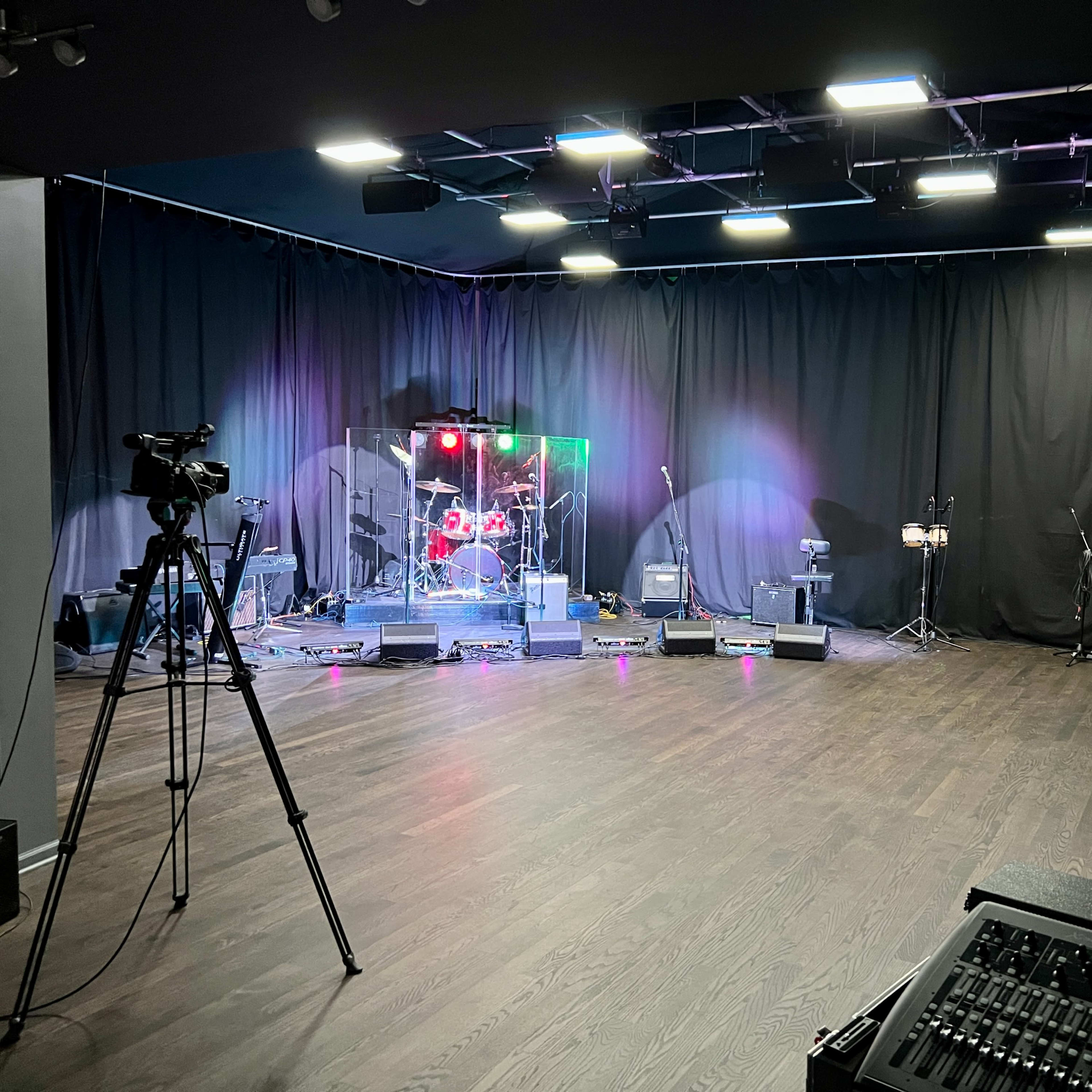 A stage setup with musical instruments, microphones, and cameras in a dimly lit room.