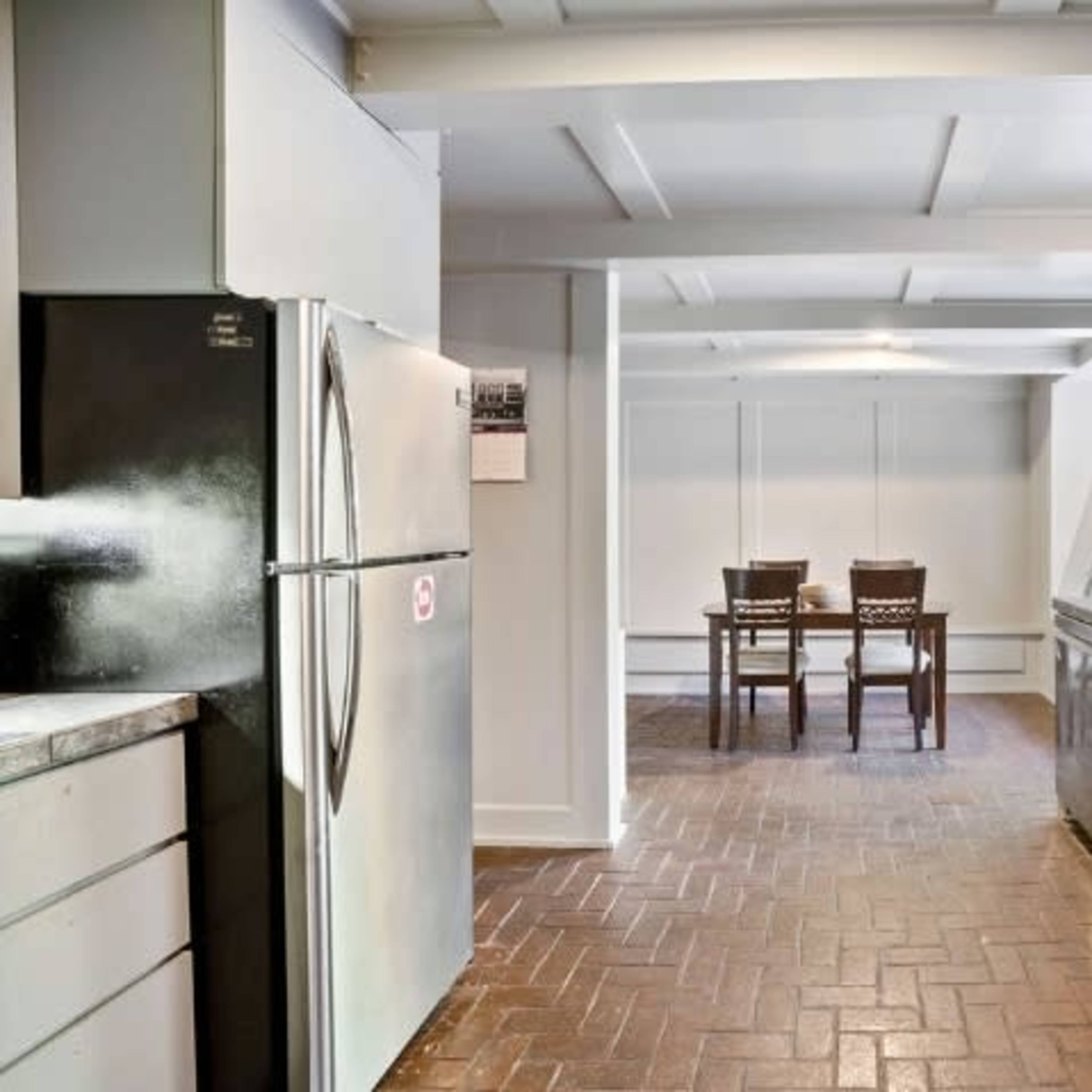 A kitchen with stainless steel appliances and a dining area featuring two wooden chairs set on a brick floor.