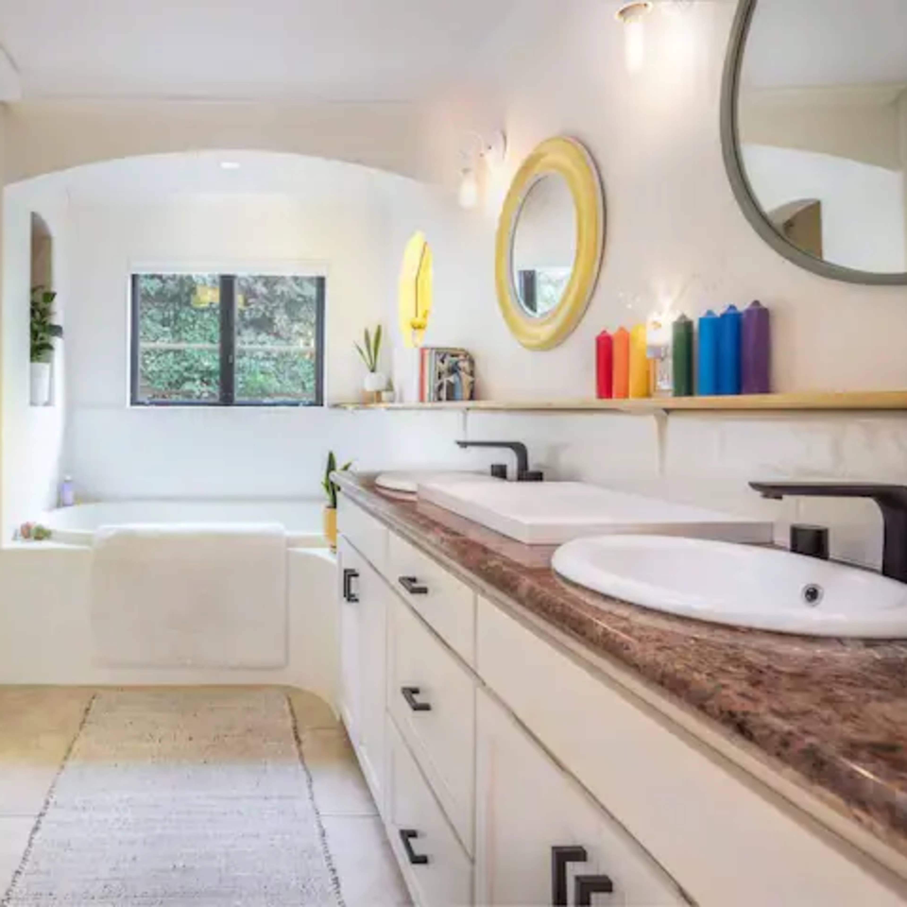 A spacious bathroom features a double sink vanity, a bathtub with a view, and colorful candles on the counter.