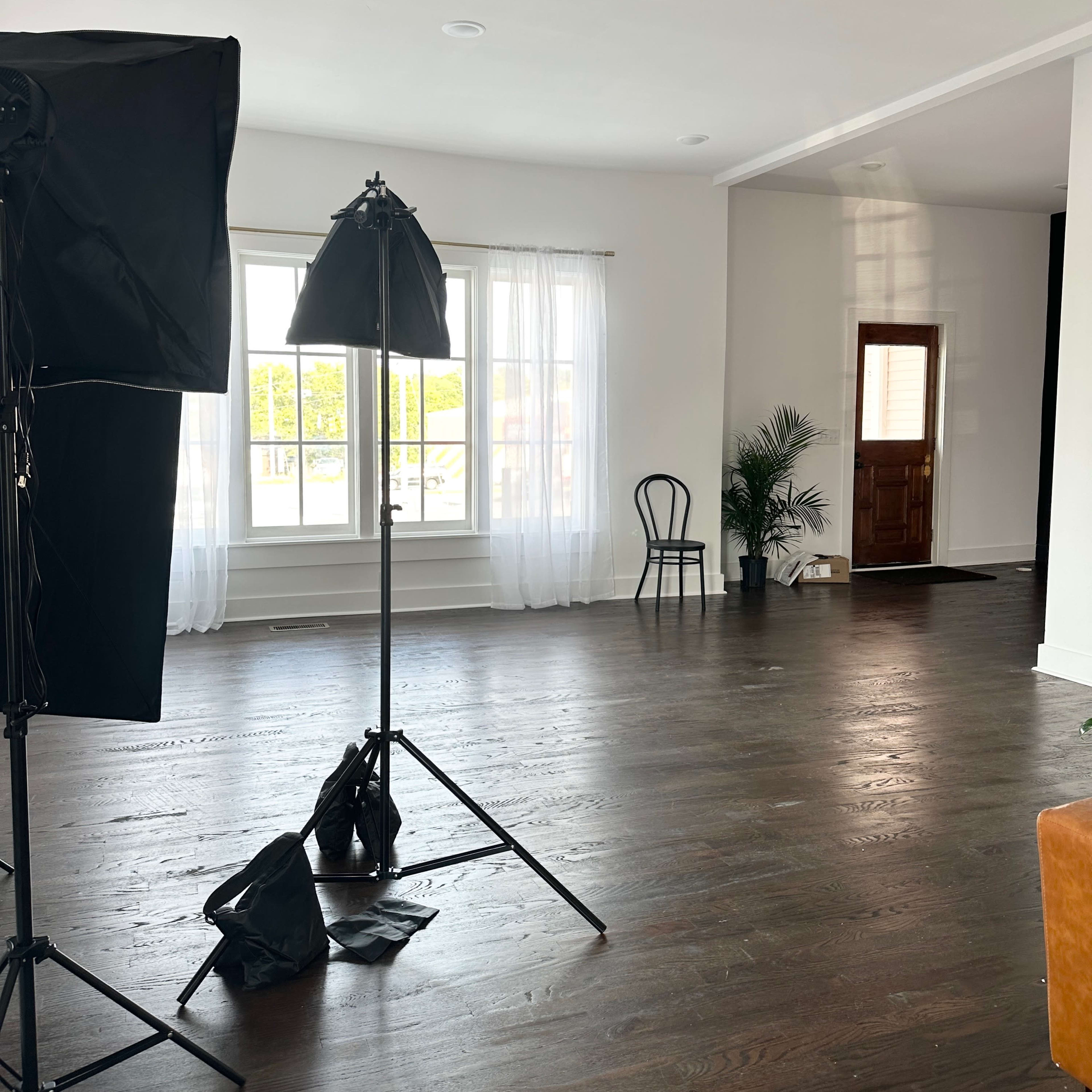 A spacious room with wooden floors, large windows, and professional lighting equipment set up.