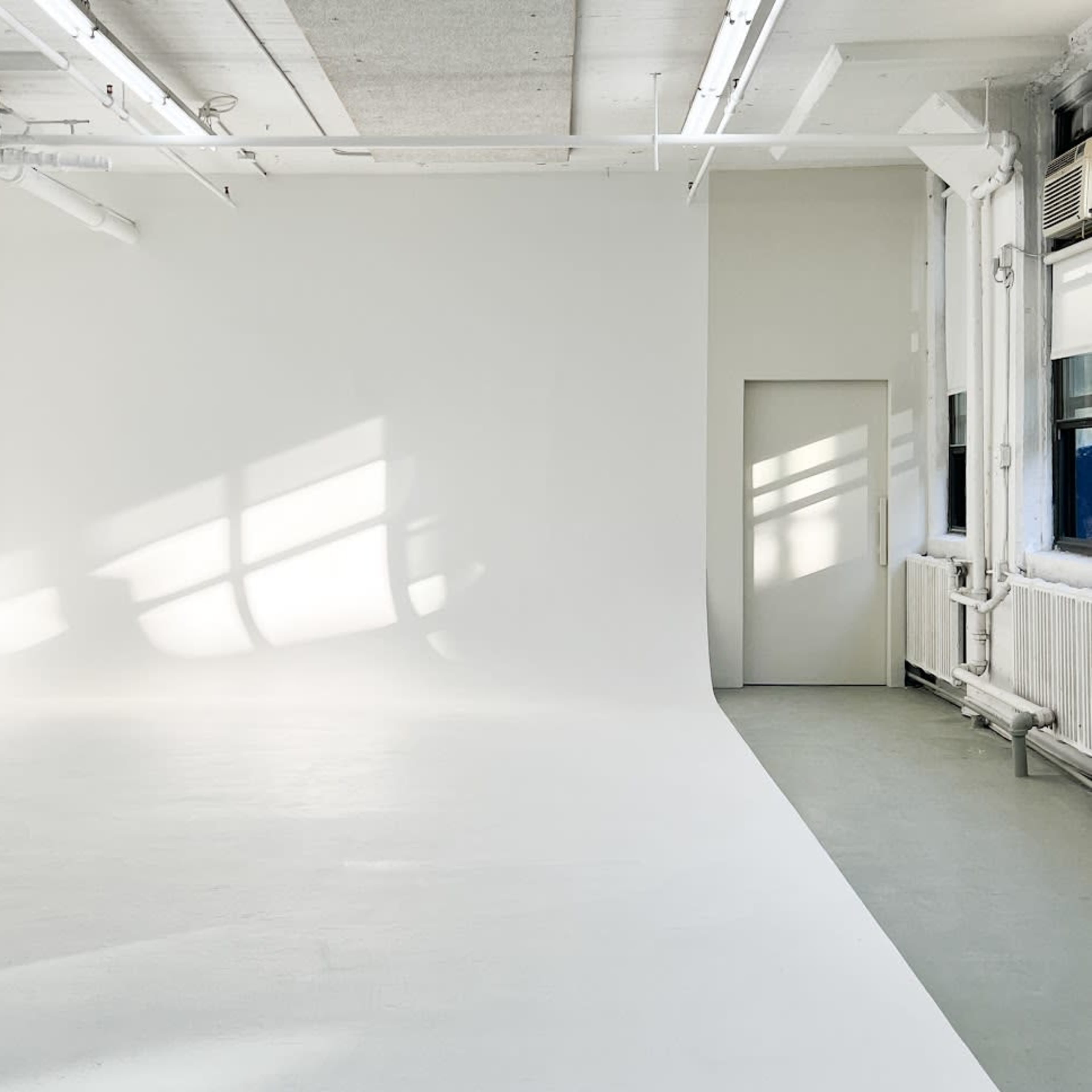 An empty, well-lit studio space with white walls and a door on the right.