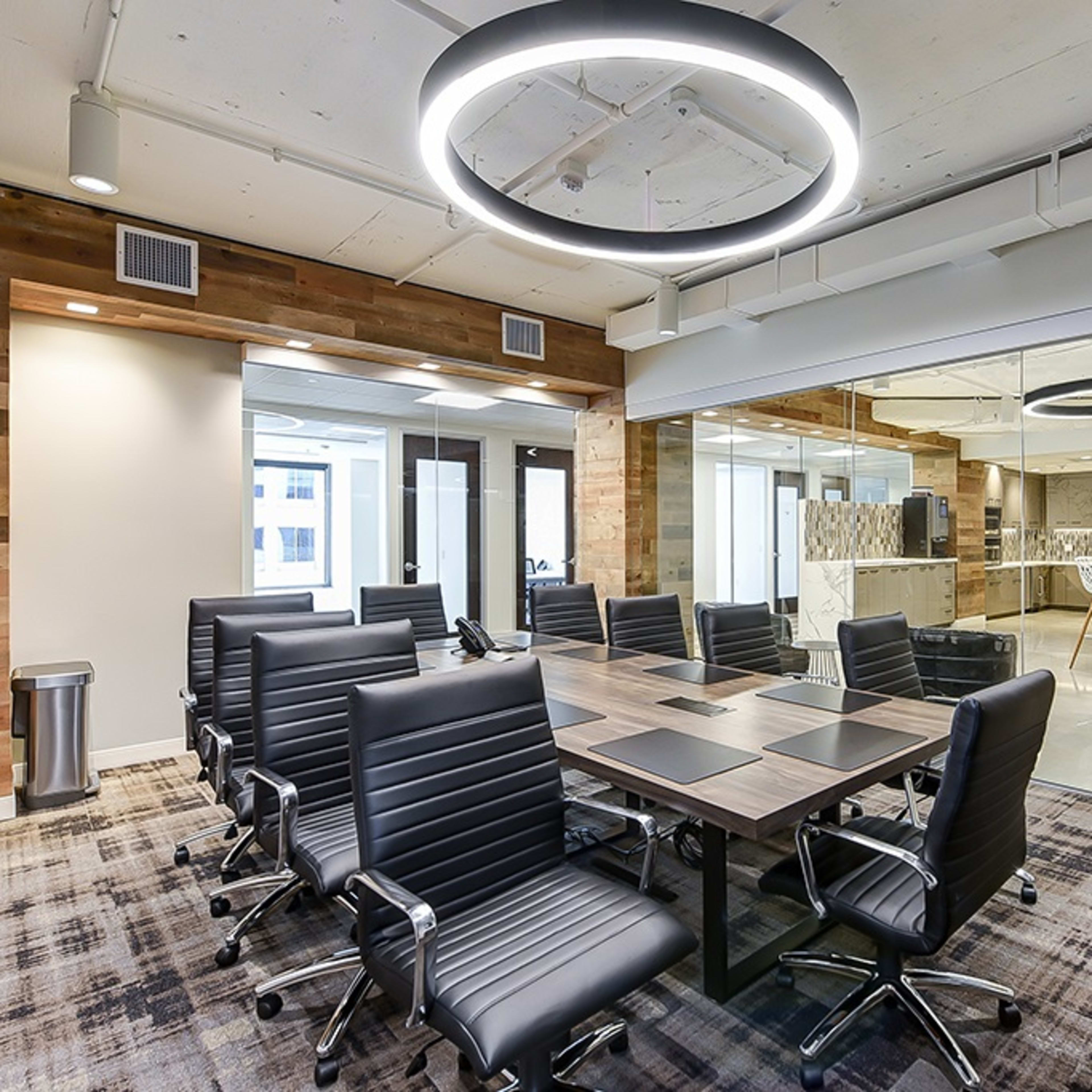 A modern conference room features a large table surrounded by ergonomic black chairs and an illuminated circular ceiling fixture.