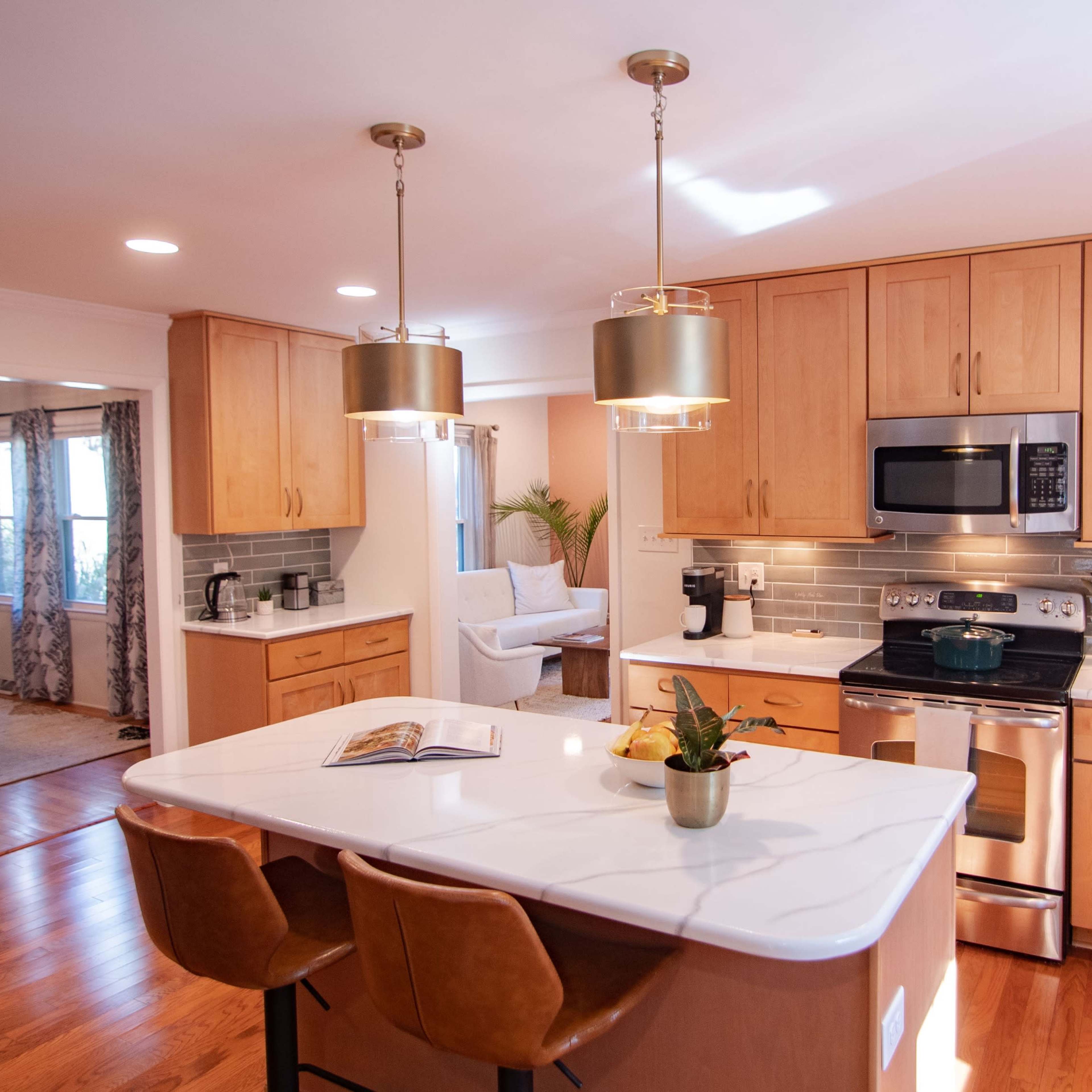 A modern kitchen features wooden cabinetry, stainless steel appliances, and a large island with bar stools and pendant lighting.