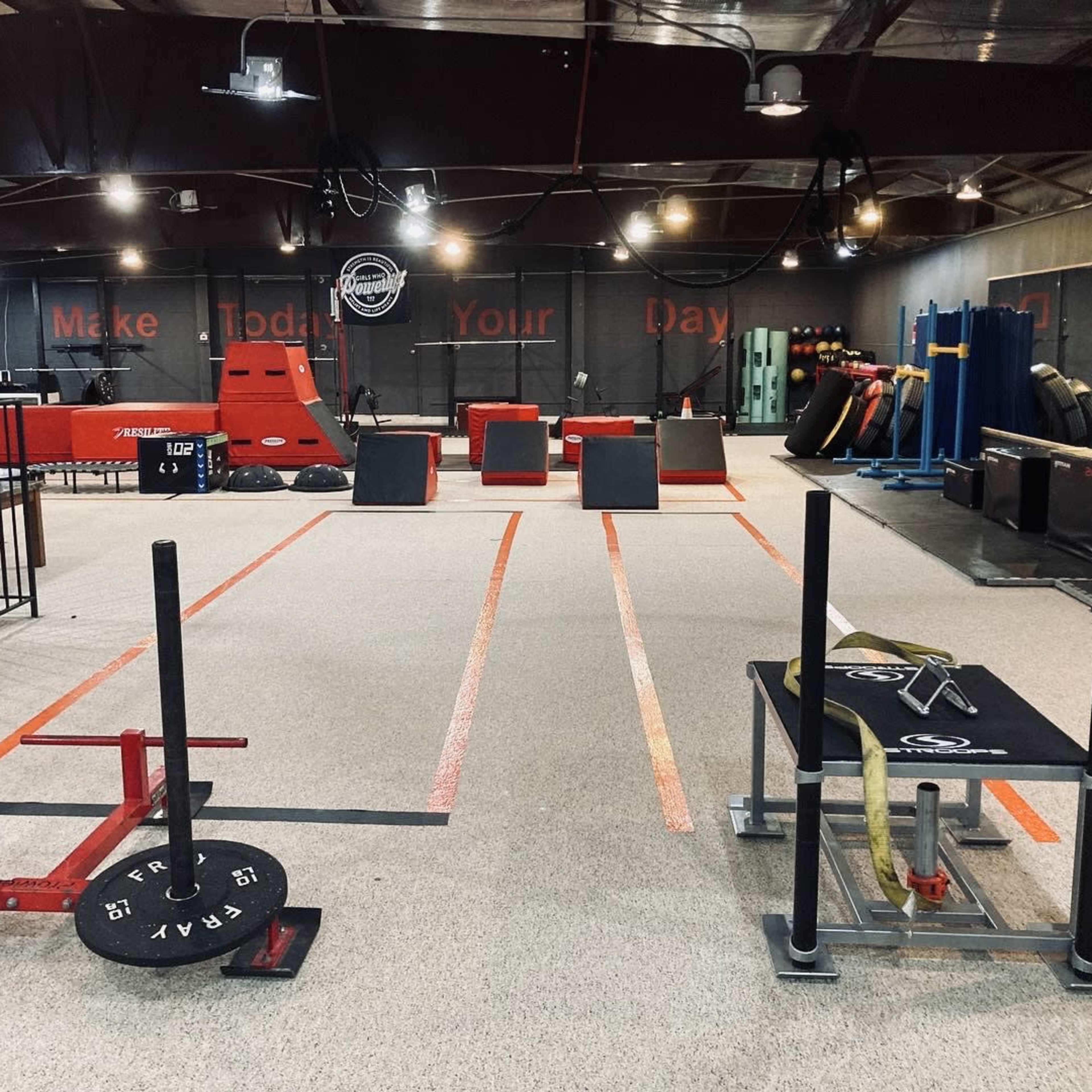 A fitness training facility with various workout equipment including weight plates, sleds, and obstacles arranged on a rubberized floor.