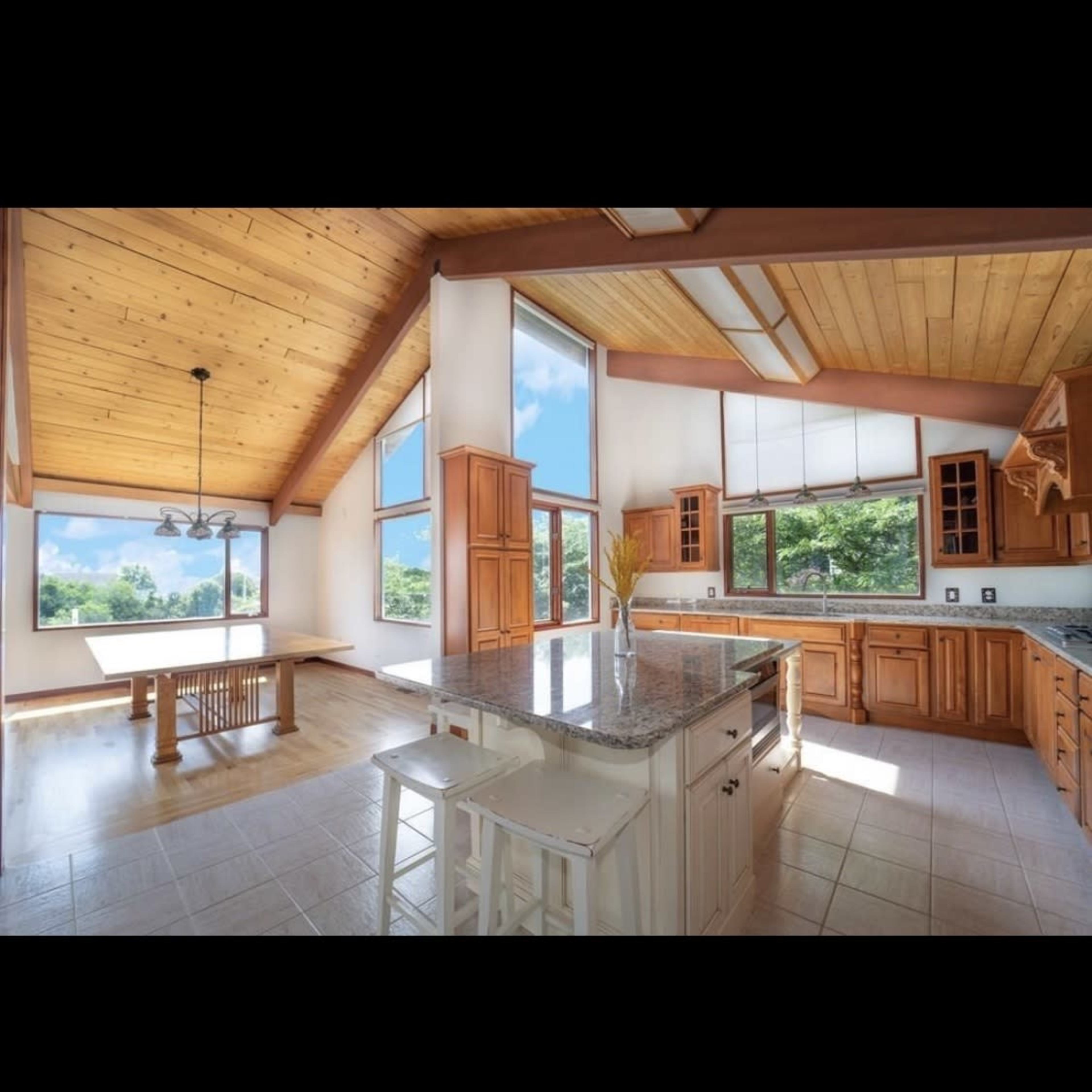 A spacious kitchen features wooden cabinets, a large island, and large windows that provide ample natural light and a view of the outdoors.