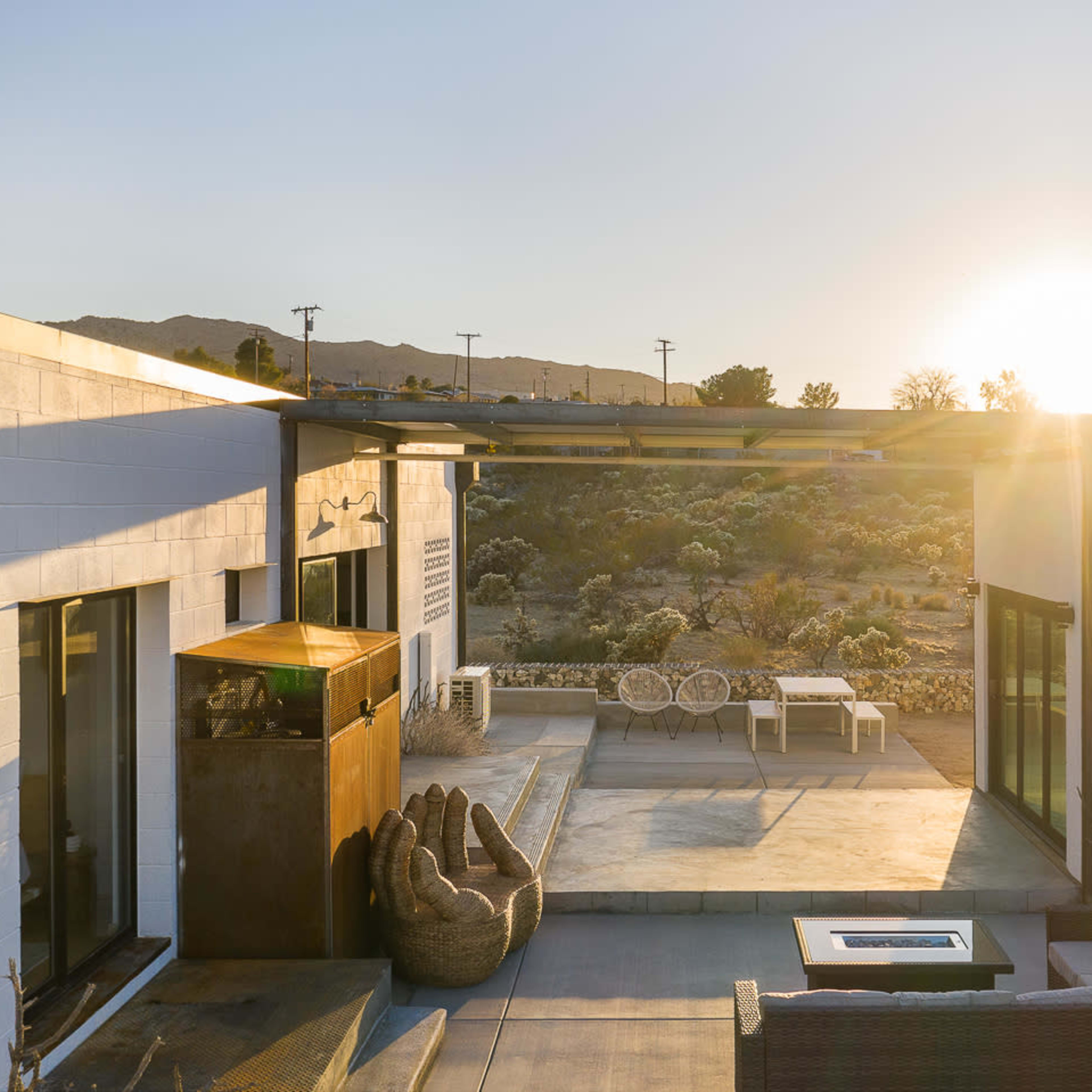 A modern architectural outdoor space with seating areas, a fire pit, and a sunset view over a desert landscape.