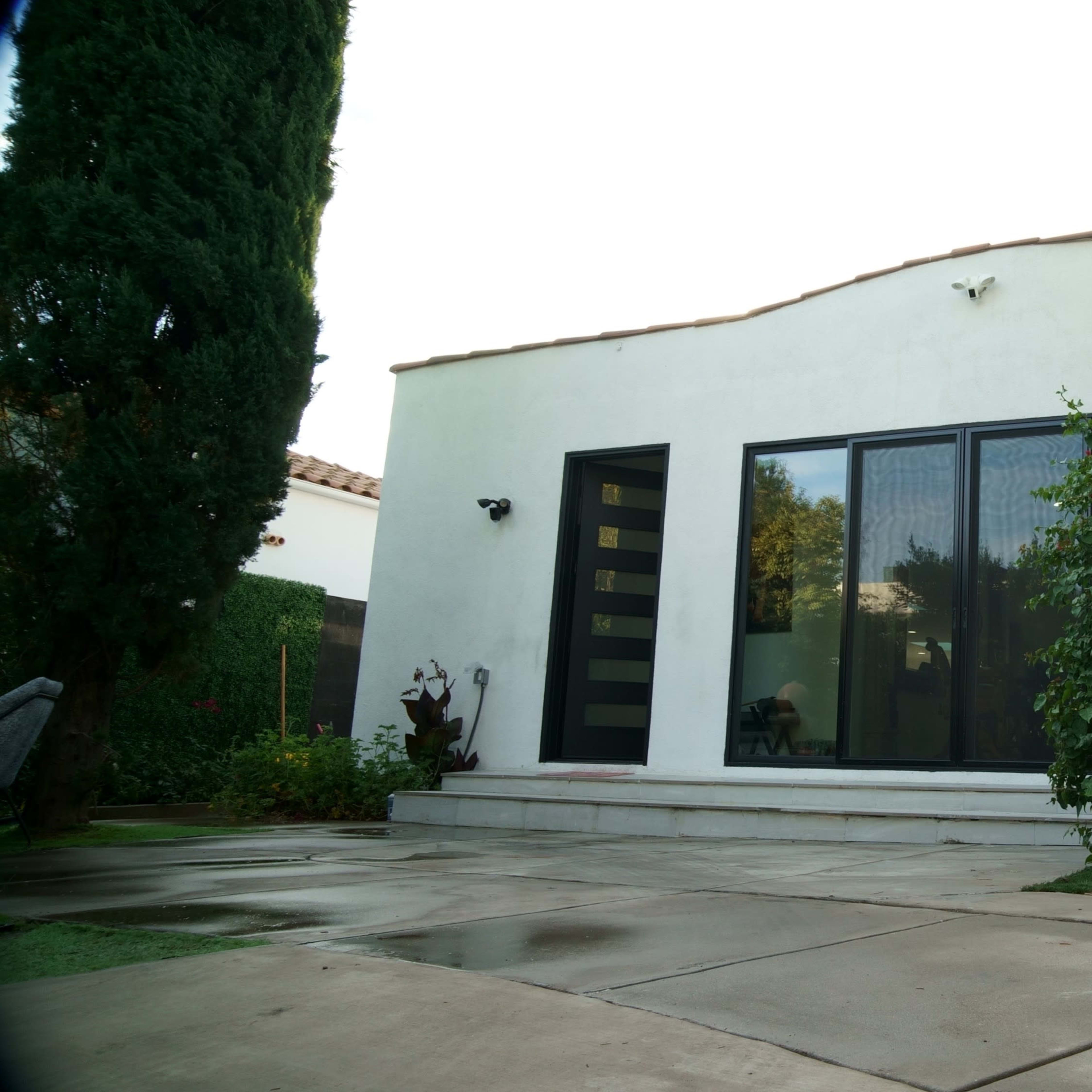 A modern house with large windows, flanked by tall cypress trees and a neatly paved driveway.