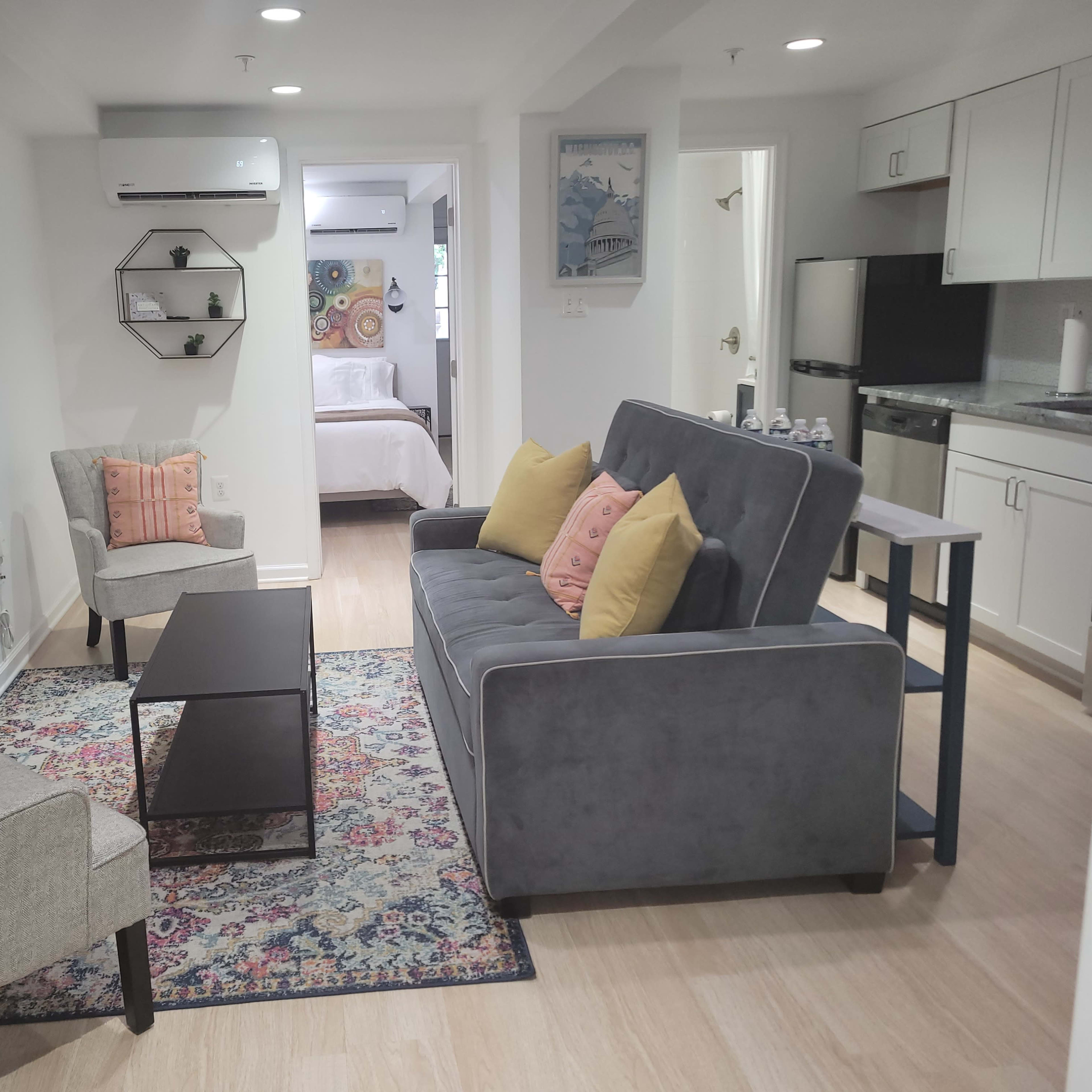 A modern living space with a gray sofa, two light-colored chairs, a coffee table, and a wall-mounted television, all arranged around a patterned rug.
