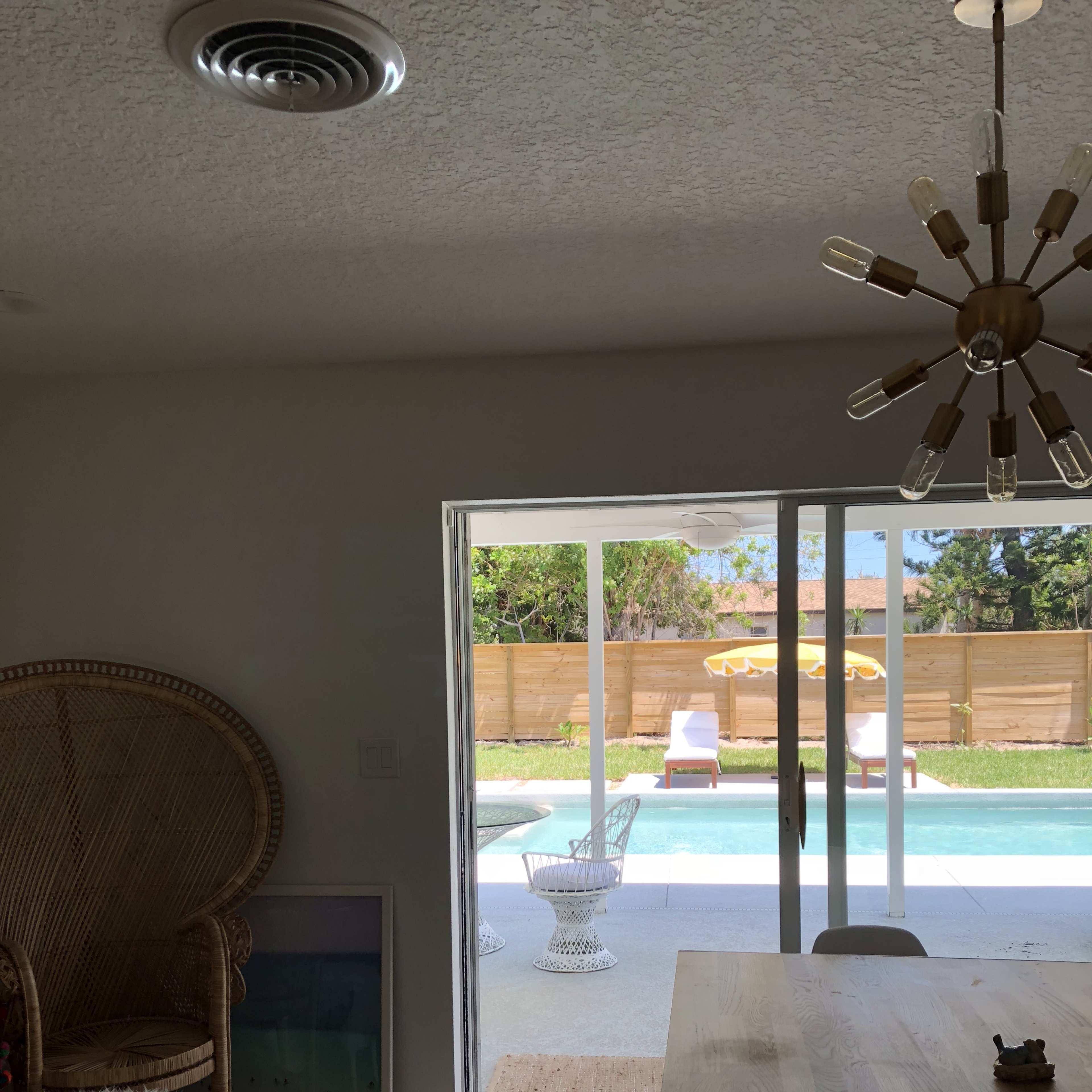 A spacious indoor area features a dining table and a large chair, with sliding glass doors opening to a patio and pool area.
