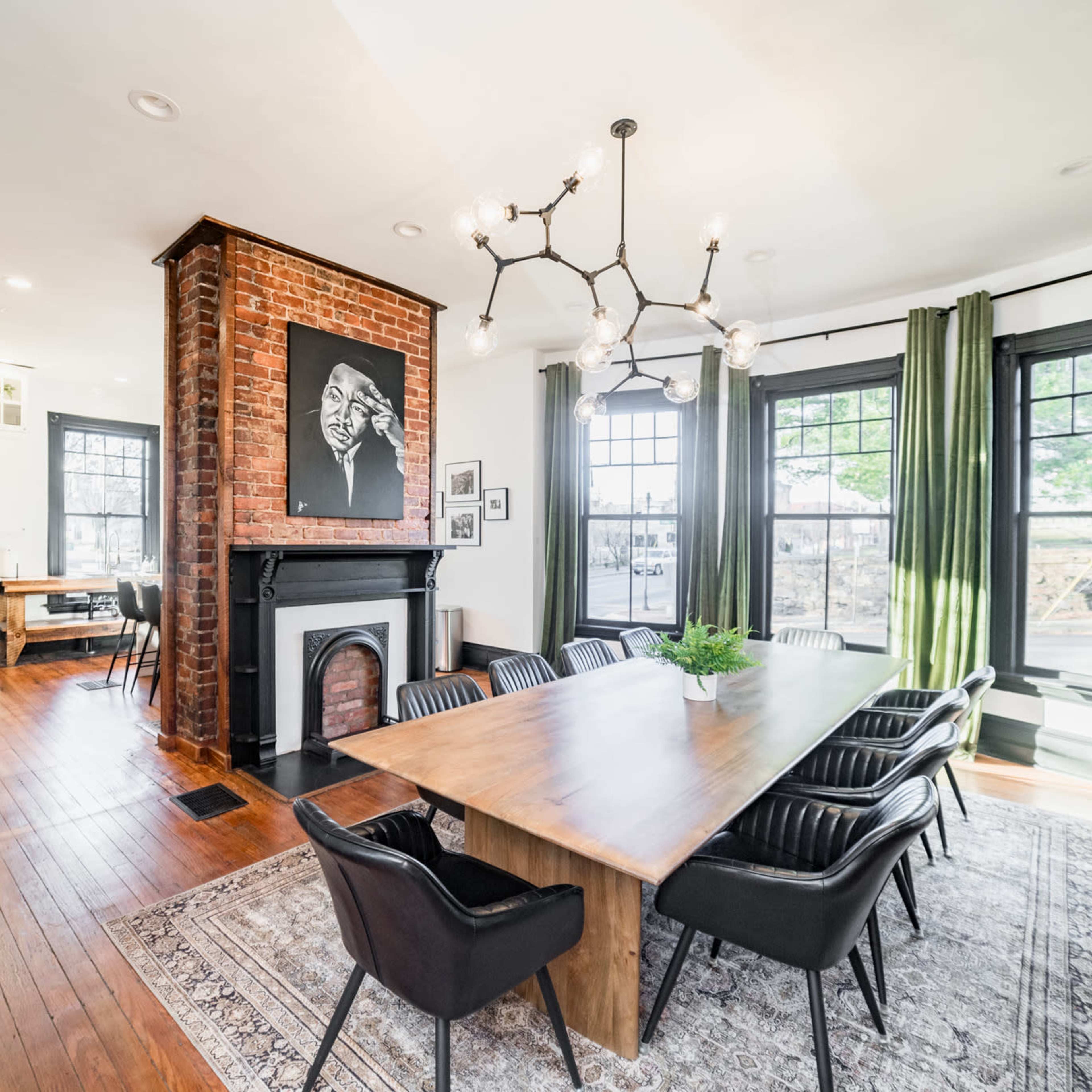 A spacious dining area featuring a large wooden table surrounded by black chairs, with a fireplace and large windows allowing natural light.