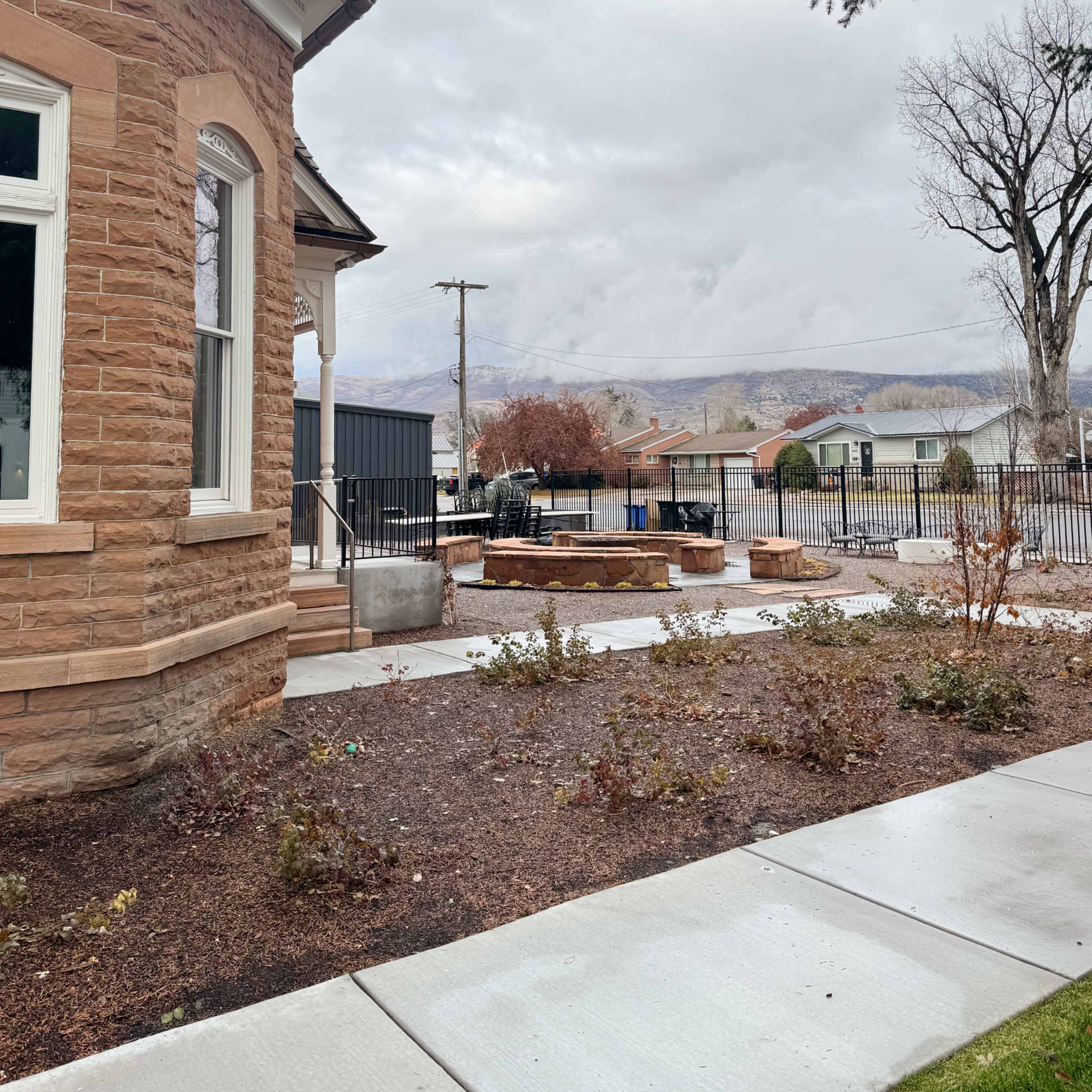 A brick house is shown with a landscaped yard, a patio area, and cloudy mountains in the background.