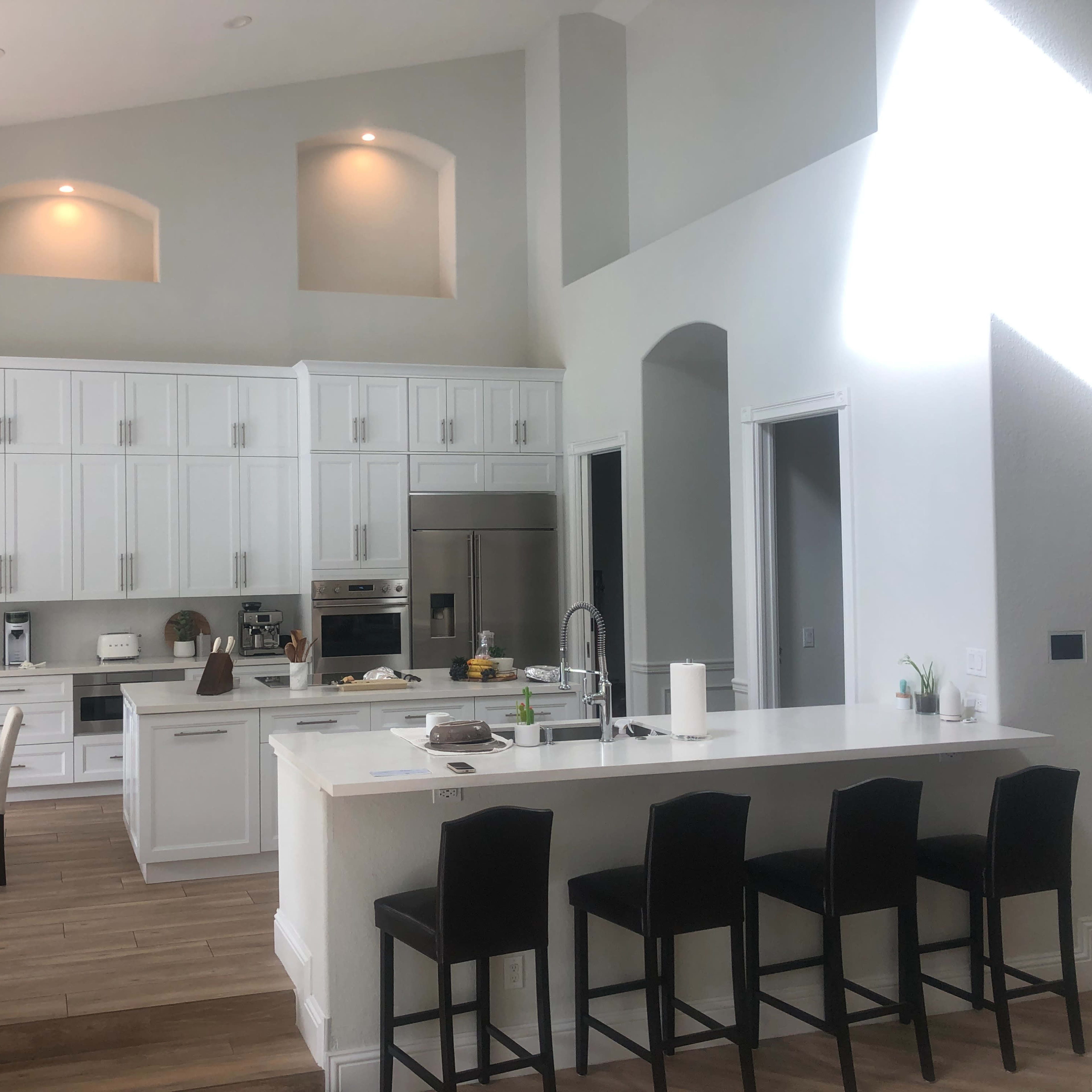 A modern kitchen with white cabinetry, a central island with seating, and a dining area featuring a round table and chairs.