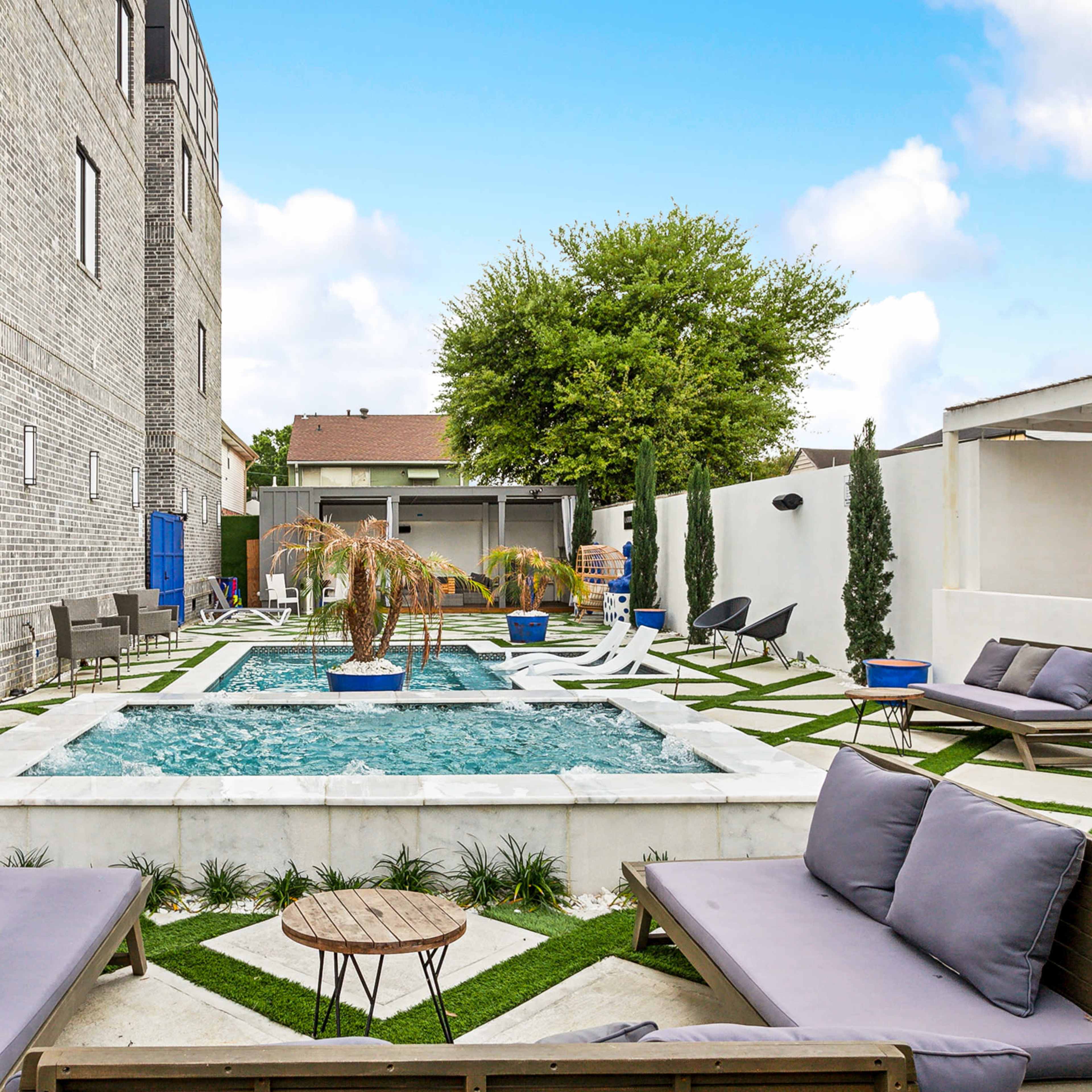 A modern outdoor space featuring a small pool surrounded by lounge chairs, a palm tree, and a well-maintained lawn.