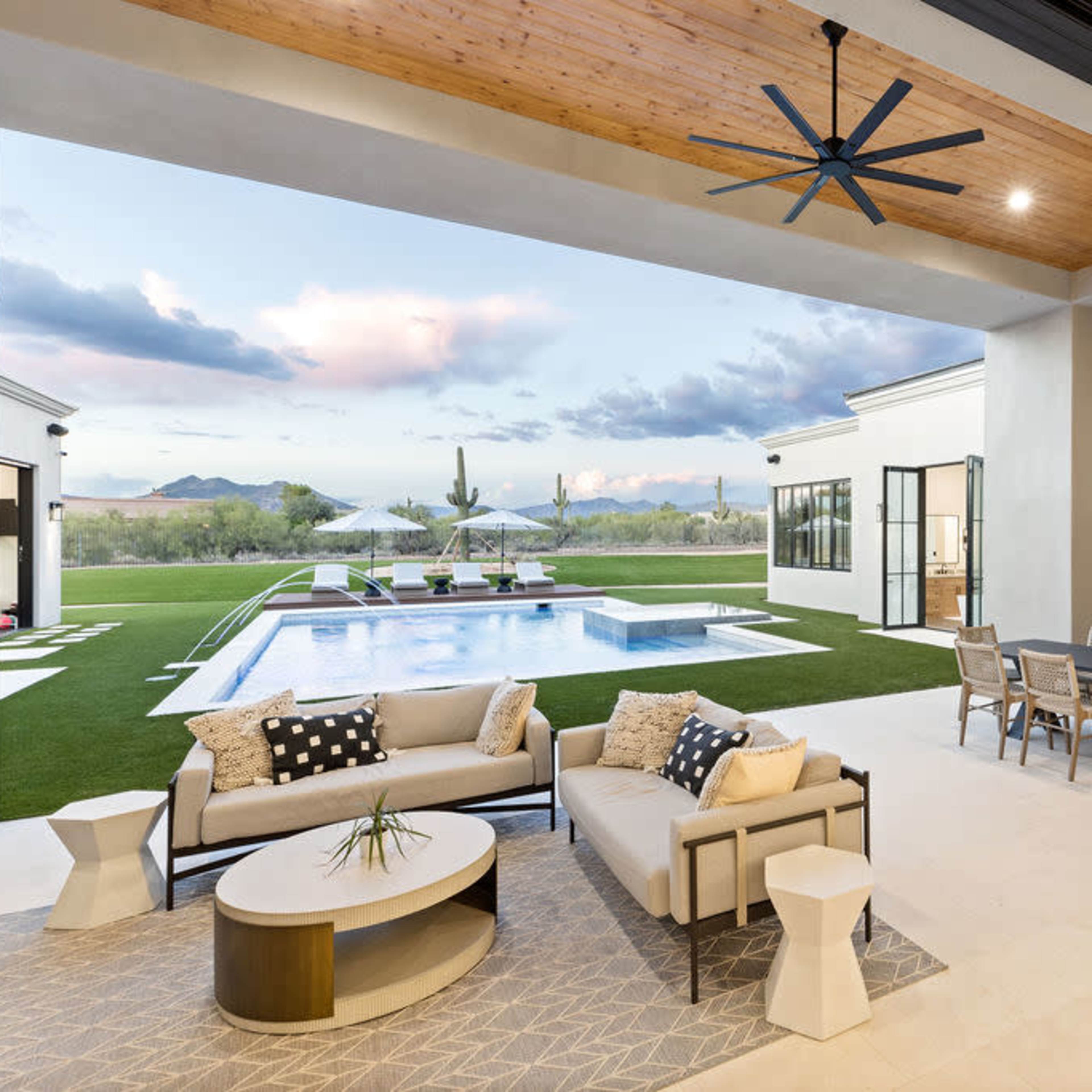A modern outdoor living space features a lounge area and dining table overlooking a pool and landscaped yard.