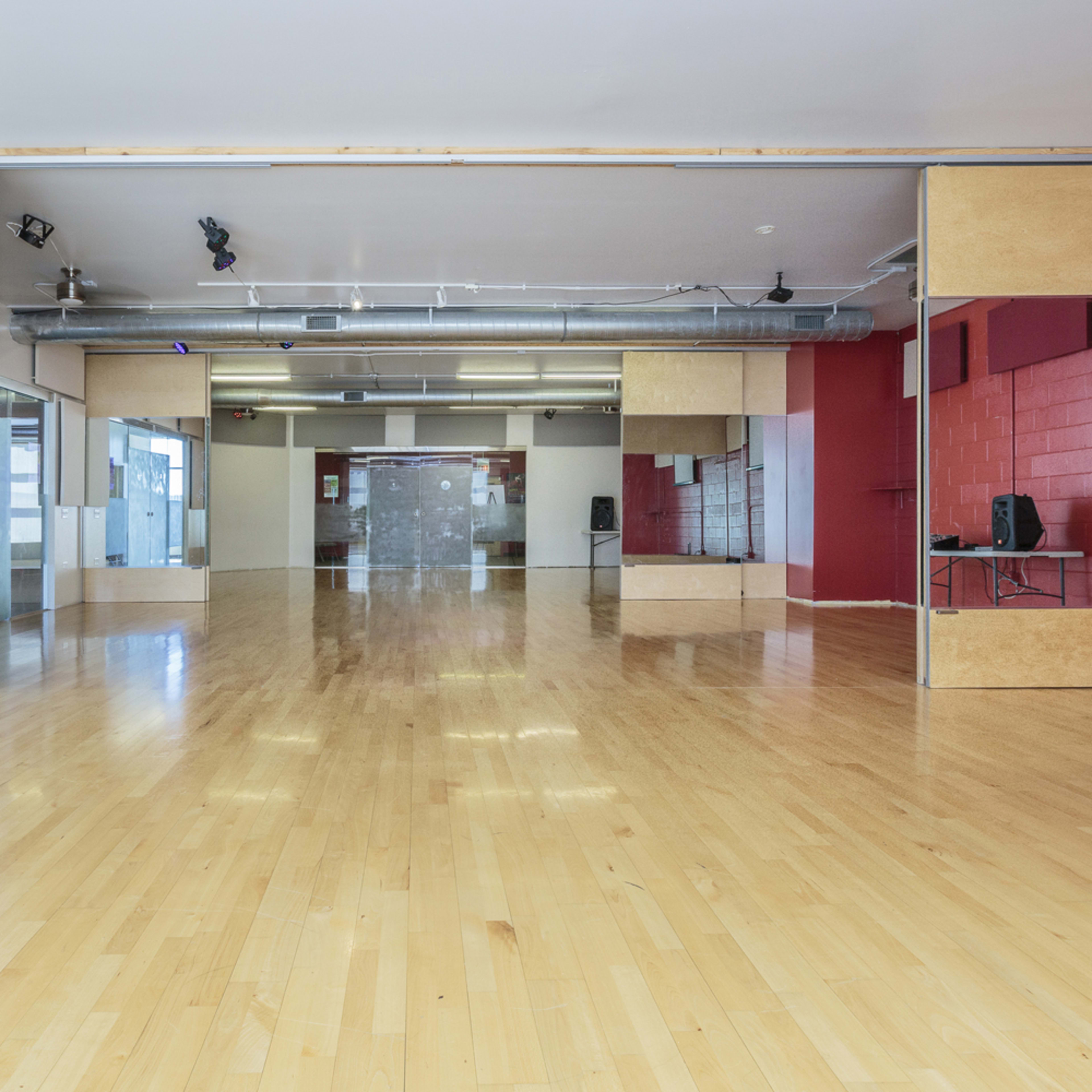 A spacious, empty dance studio with wooden floors, mirrored walls, and red and gray accent colors.