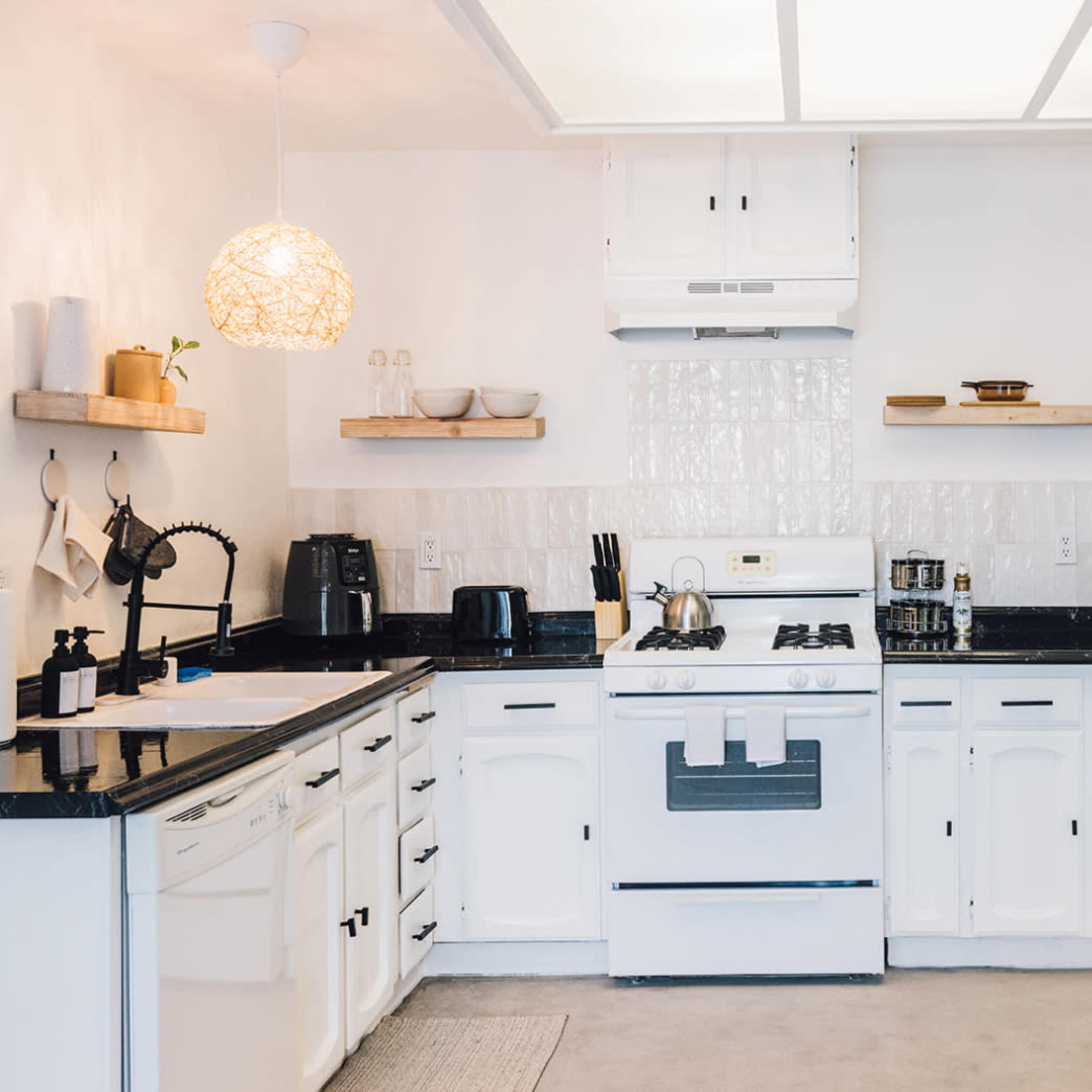 A clean kitchen features white cabinets, black countertops, and an organized layout with shelves displaying cooking utensils and decorative items.
