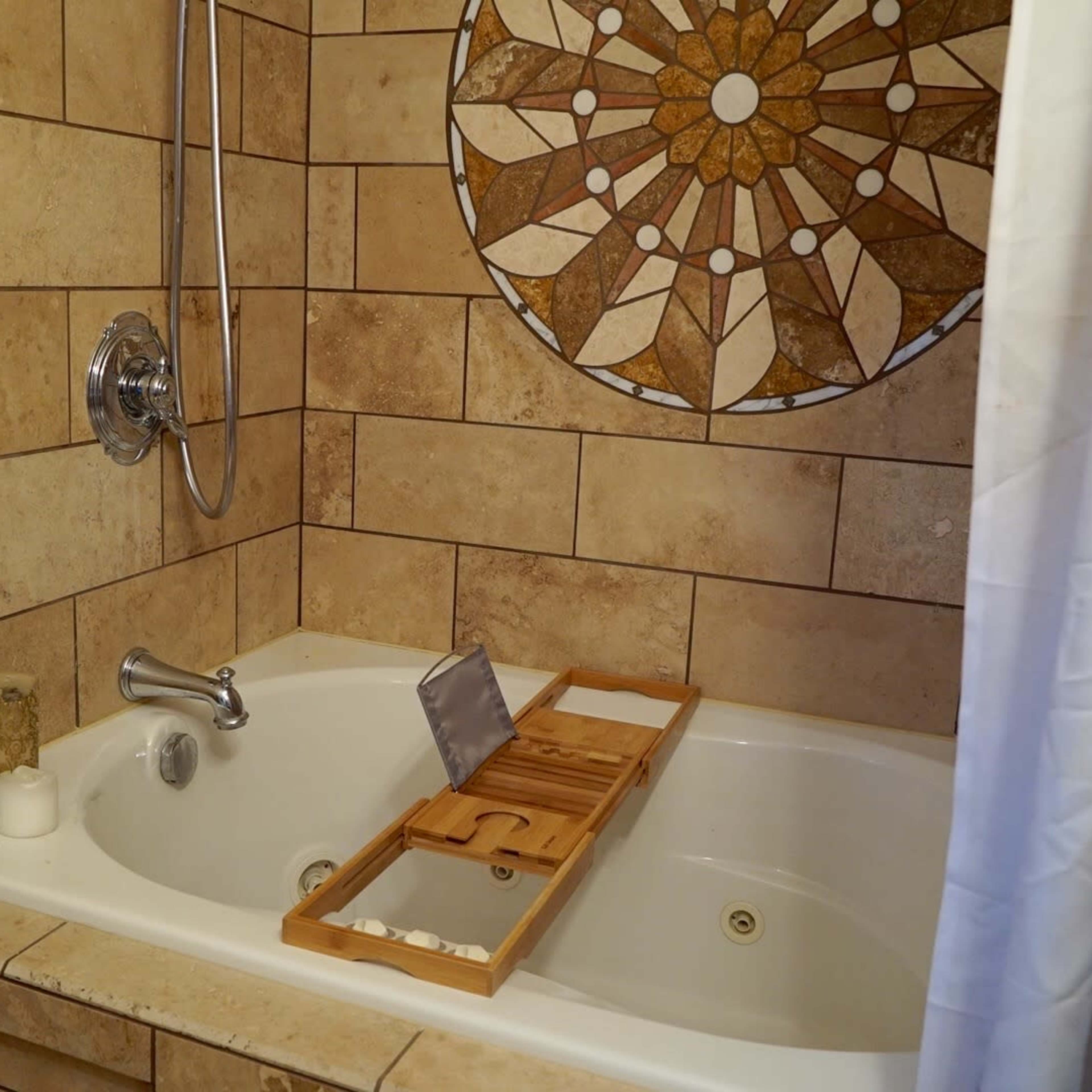 A bathtub with a wooden tray across it, featuring a decorative mosaic on the wall behind.