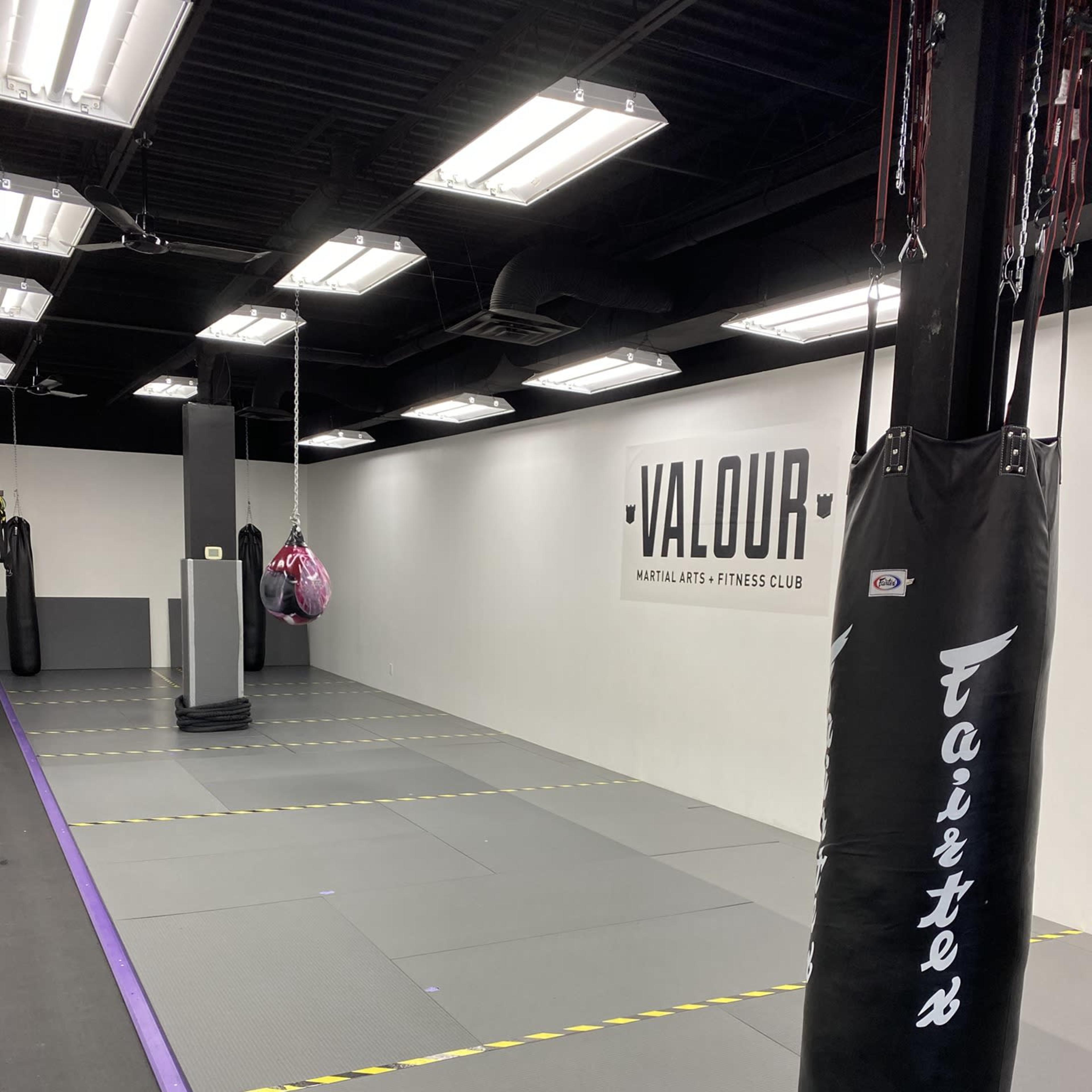 An empty martial arts gym with padded flooring, a punching bag, and a wall displaying the word "VALOUR."
