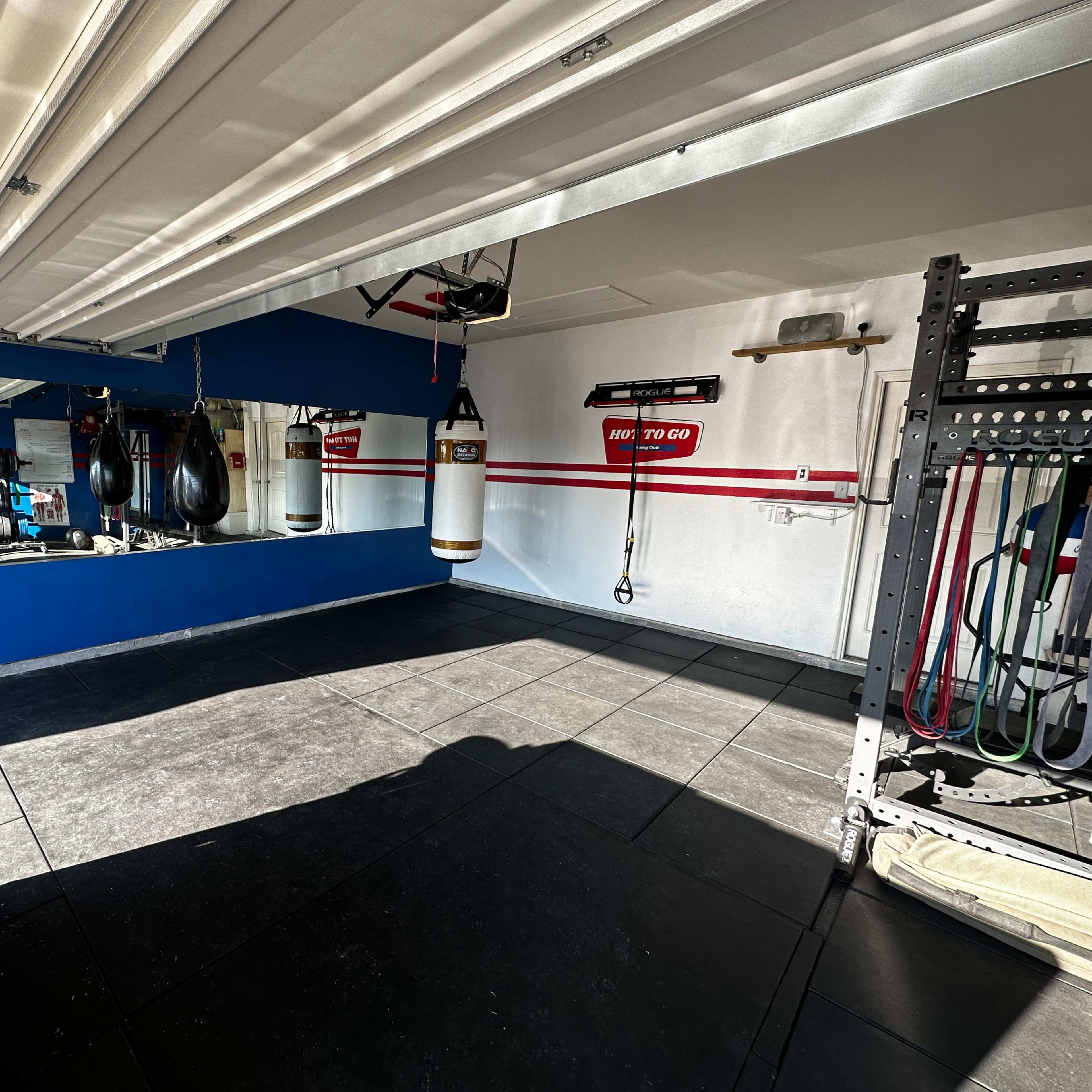 A home gym with weights, a boxing bag, and a mirror against a blue wall, featuring red stripes.