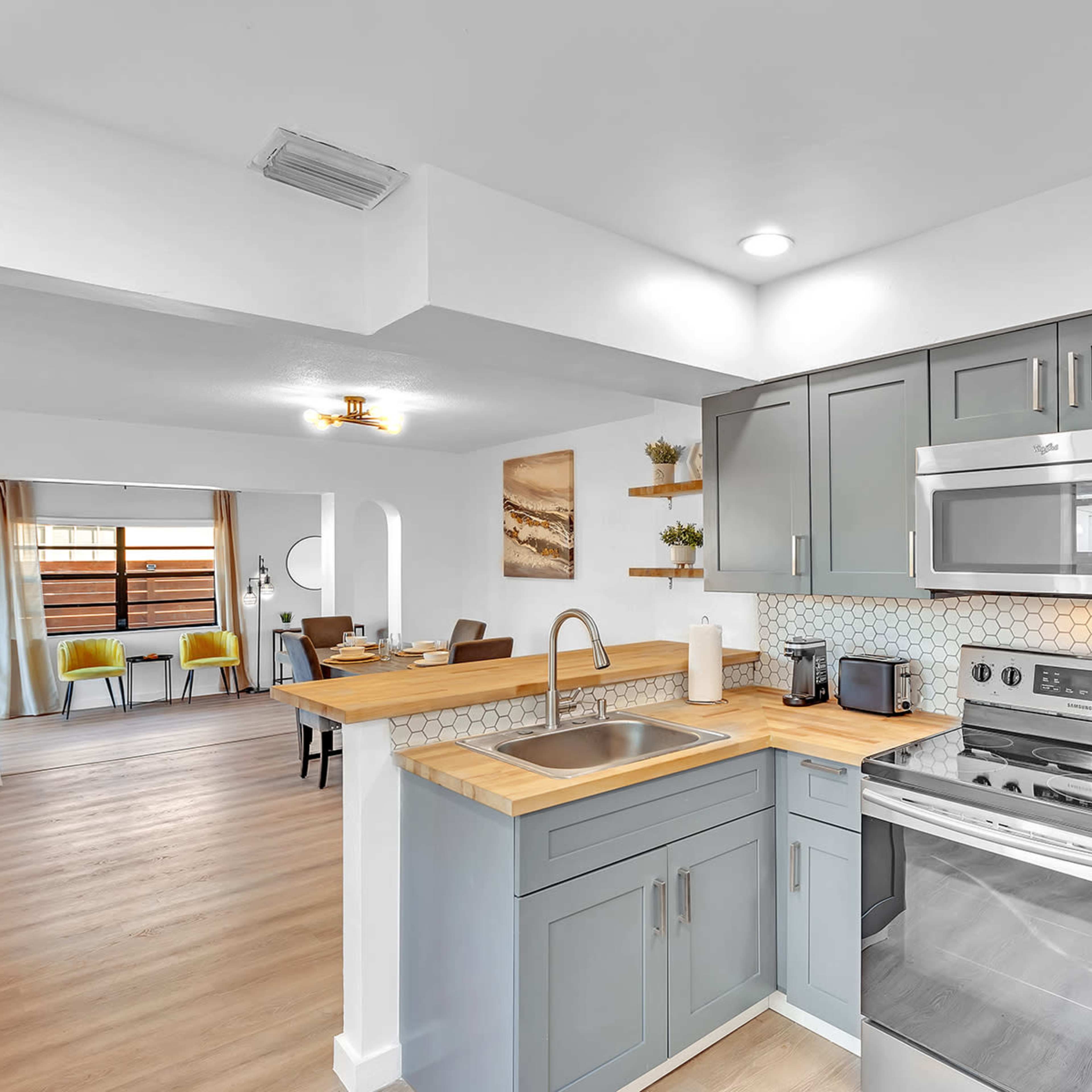 A modern kitchen features gray cabinets, stainless steel appliances, and a wooden countertop, with an open layout leading to a dining area.