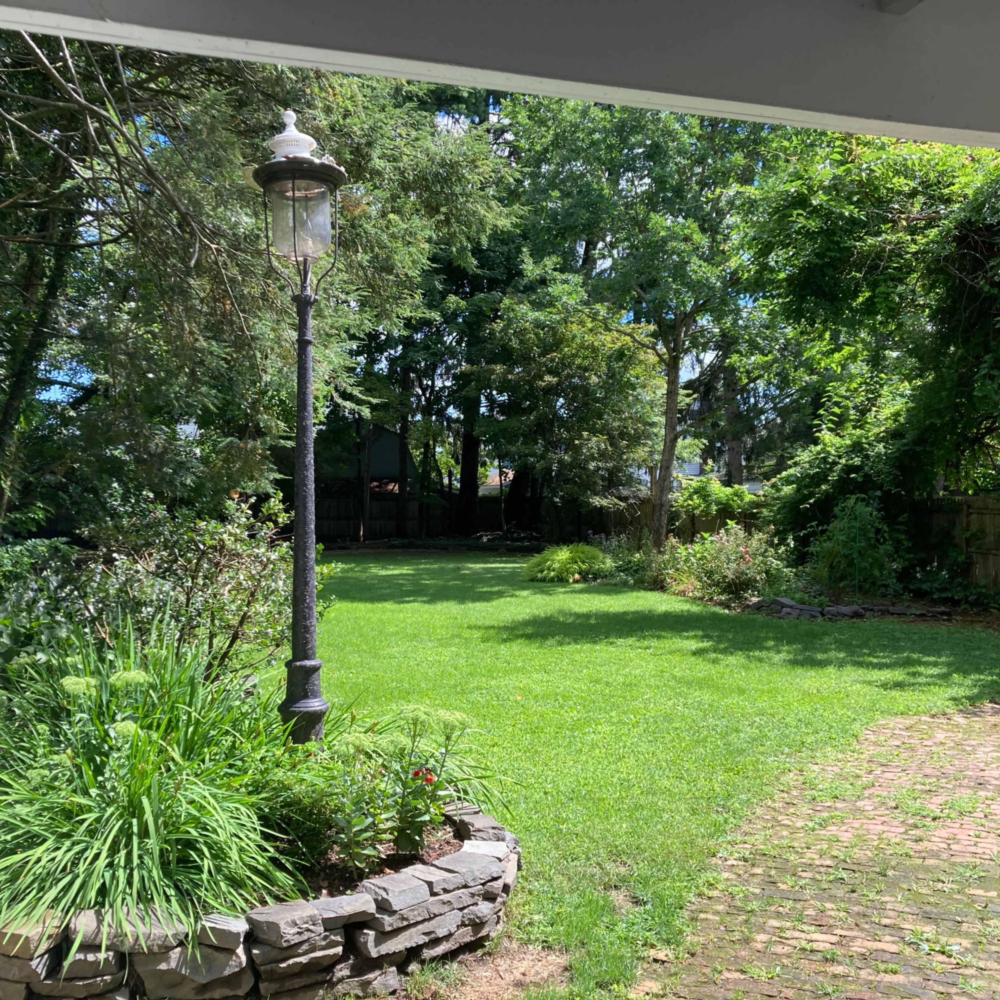 A well-maintained backyard features a grassy area, a stone pathway, and a decorative lamp post surrounded by greenery.