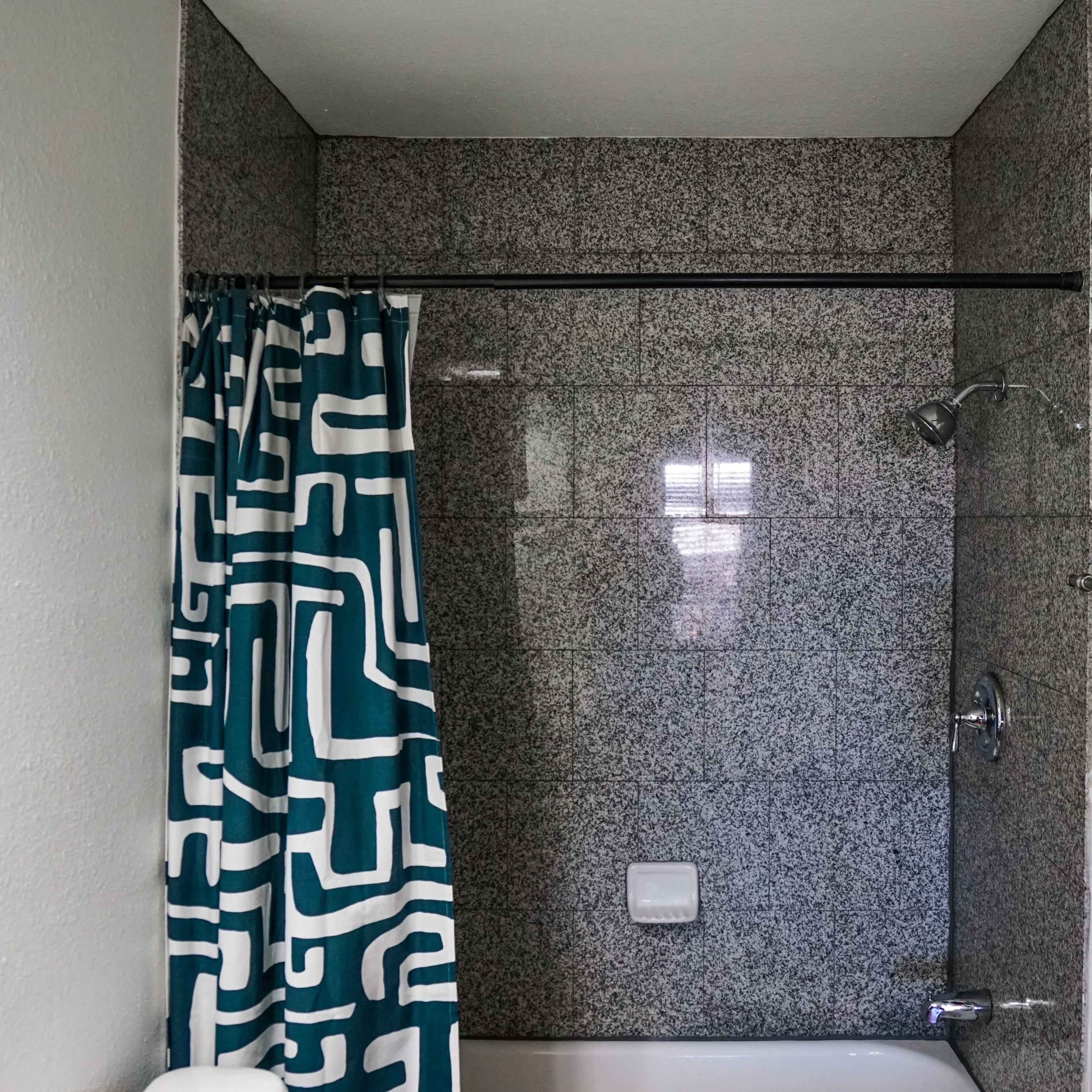 A modern bathroom with a bathtub, a patterned shower curtain, and a blue towel hanging on a rack.