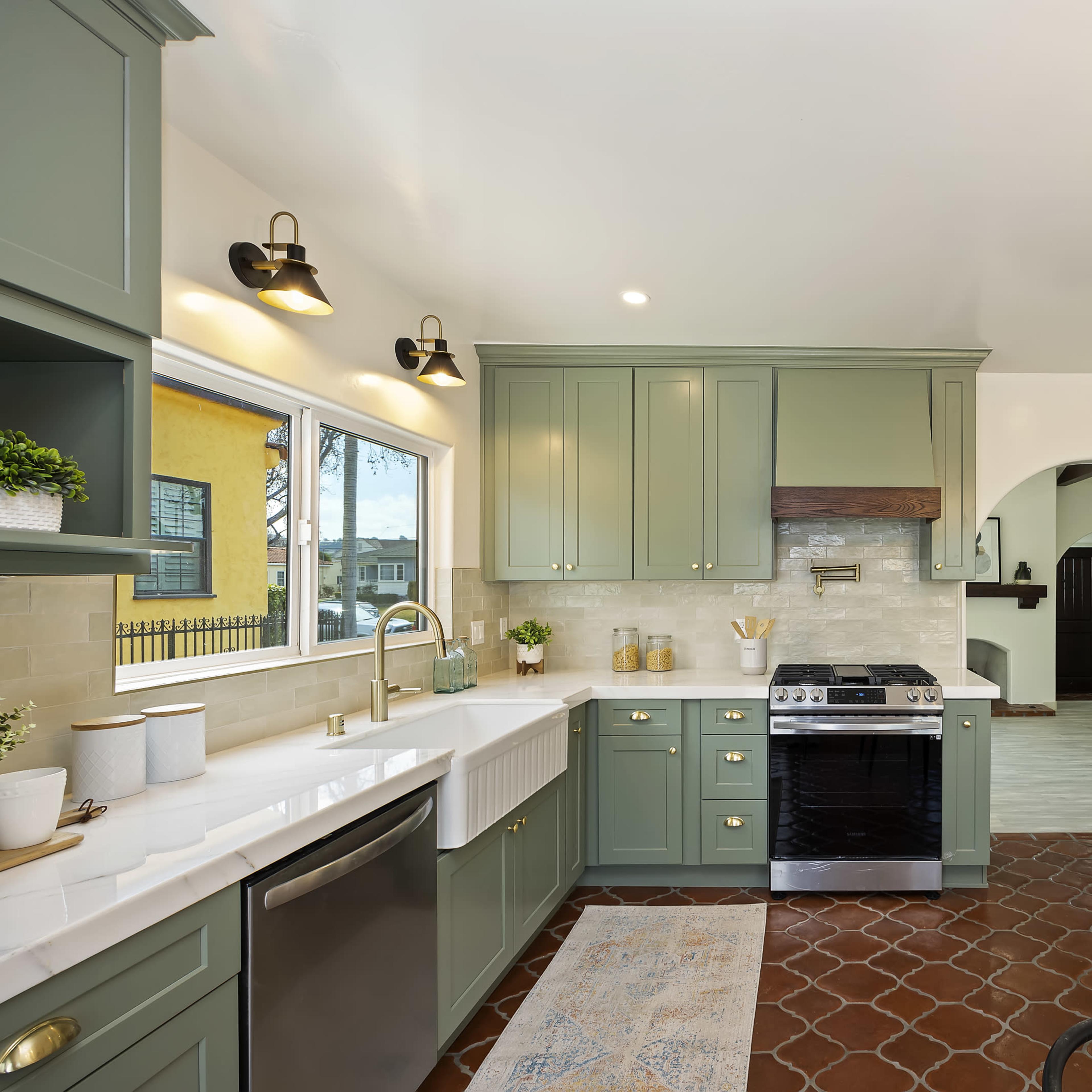 A modern kitchen features green cabinetry, stainless steel appliances, and a farmhouse sink with a tile backsplash.