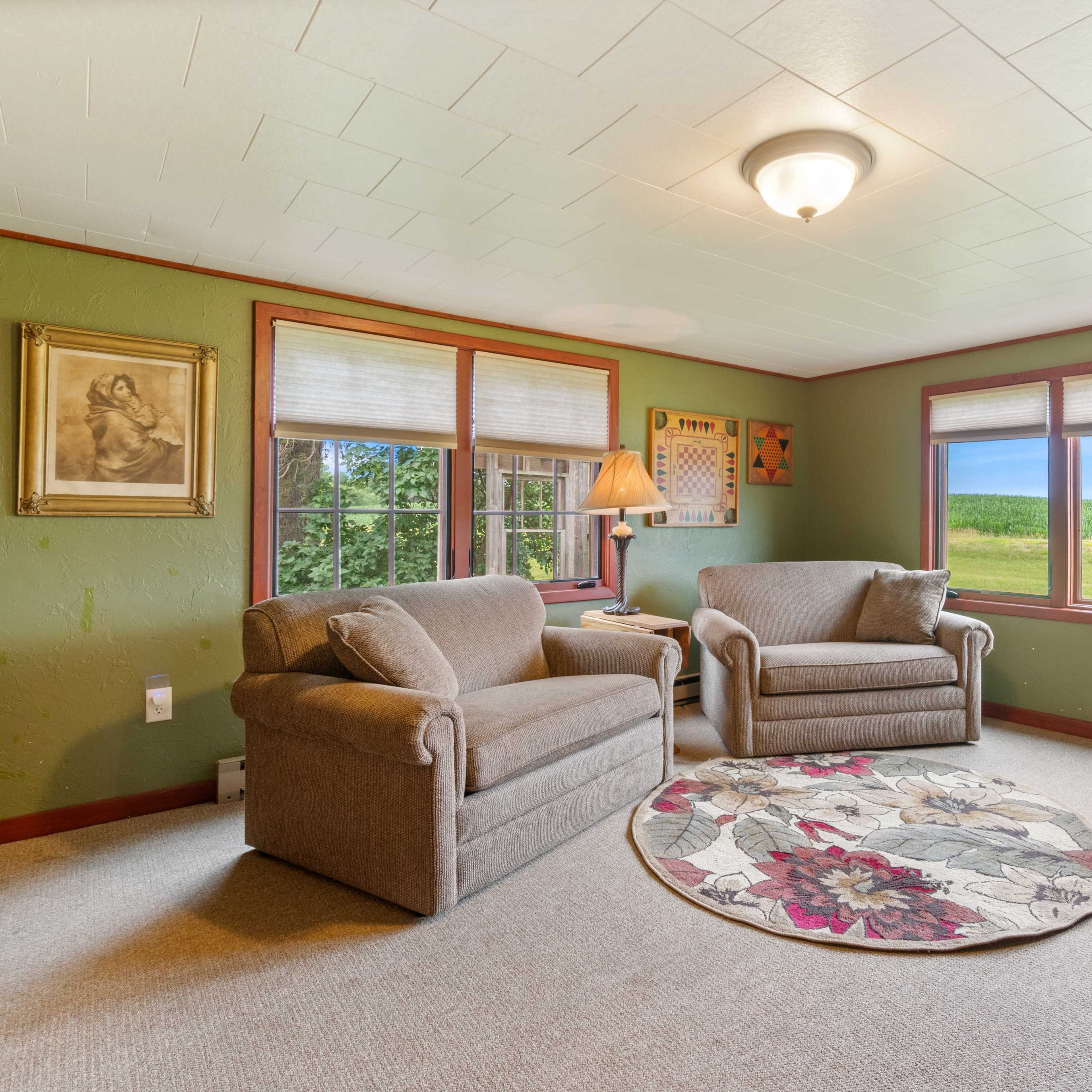 A cozy room with two chairs, a round rug, and large windows overlooking a green field.