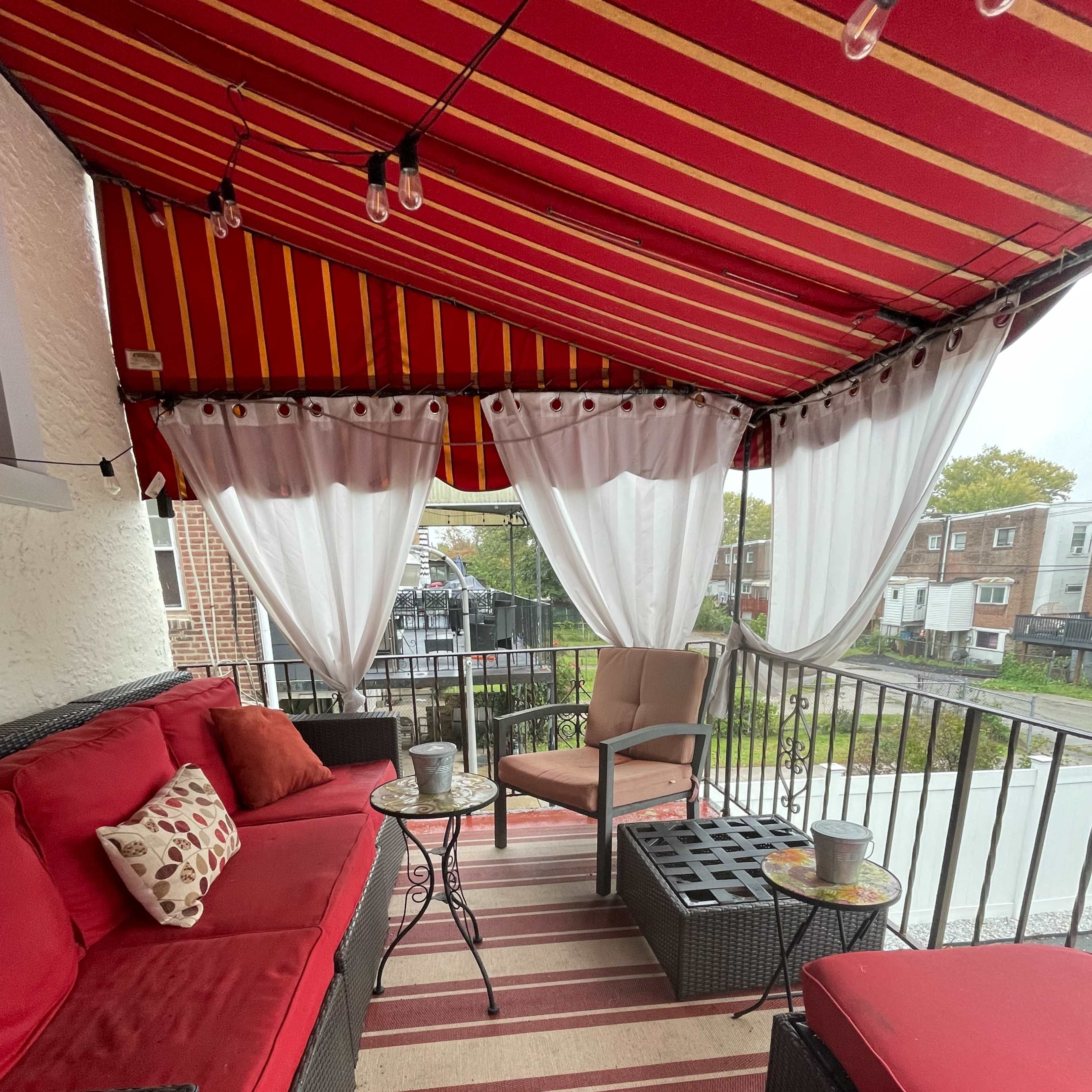 A covered outdoor porch with red and yellow striped awnings, featuring a seating area with red cushions and a small table.