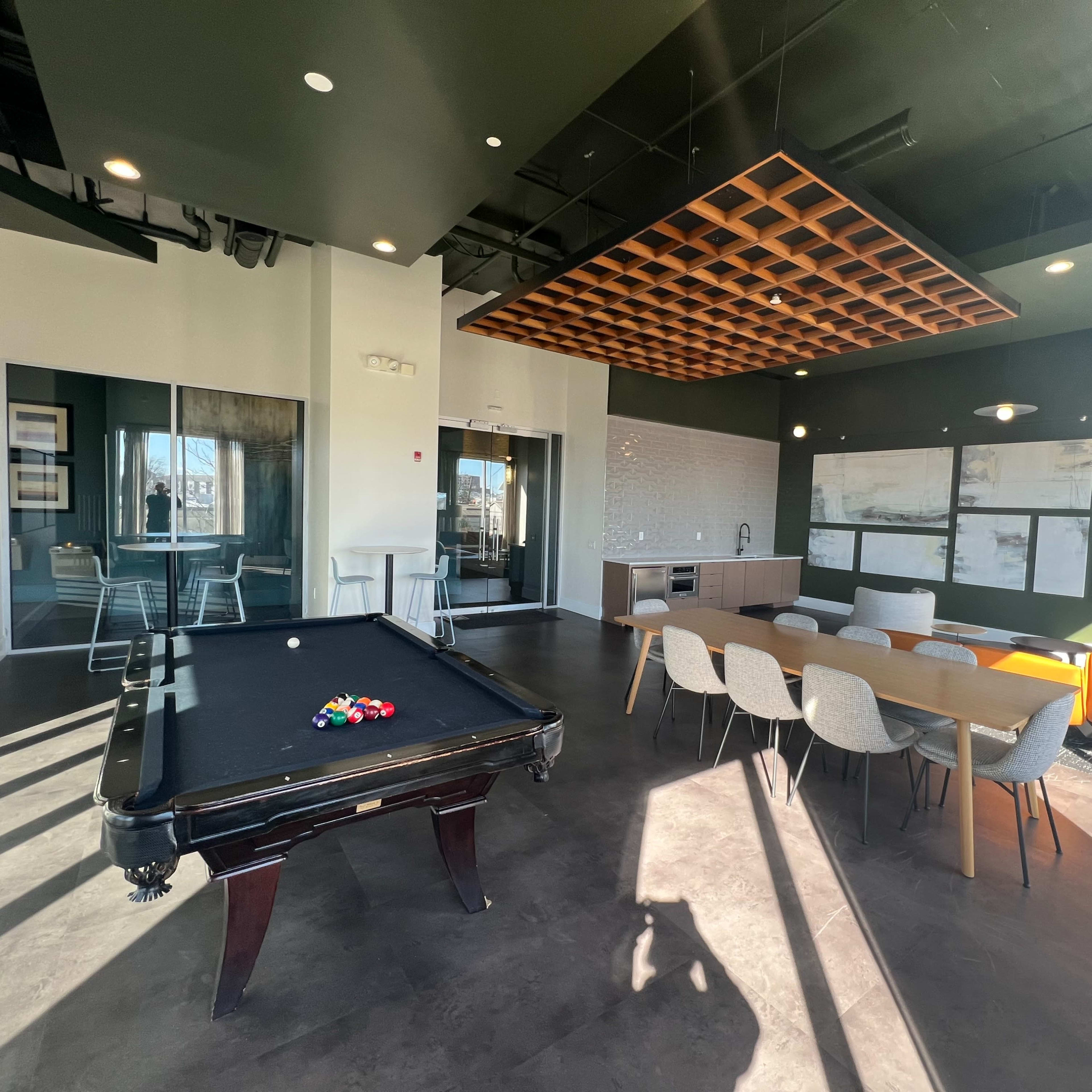 A modern communal lounge featuring a billiard table, a dining area with chairs, and a cozy seating arrangement.