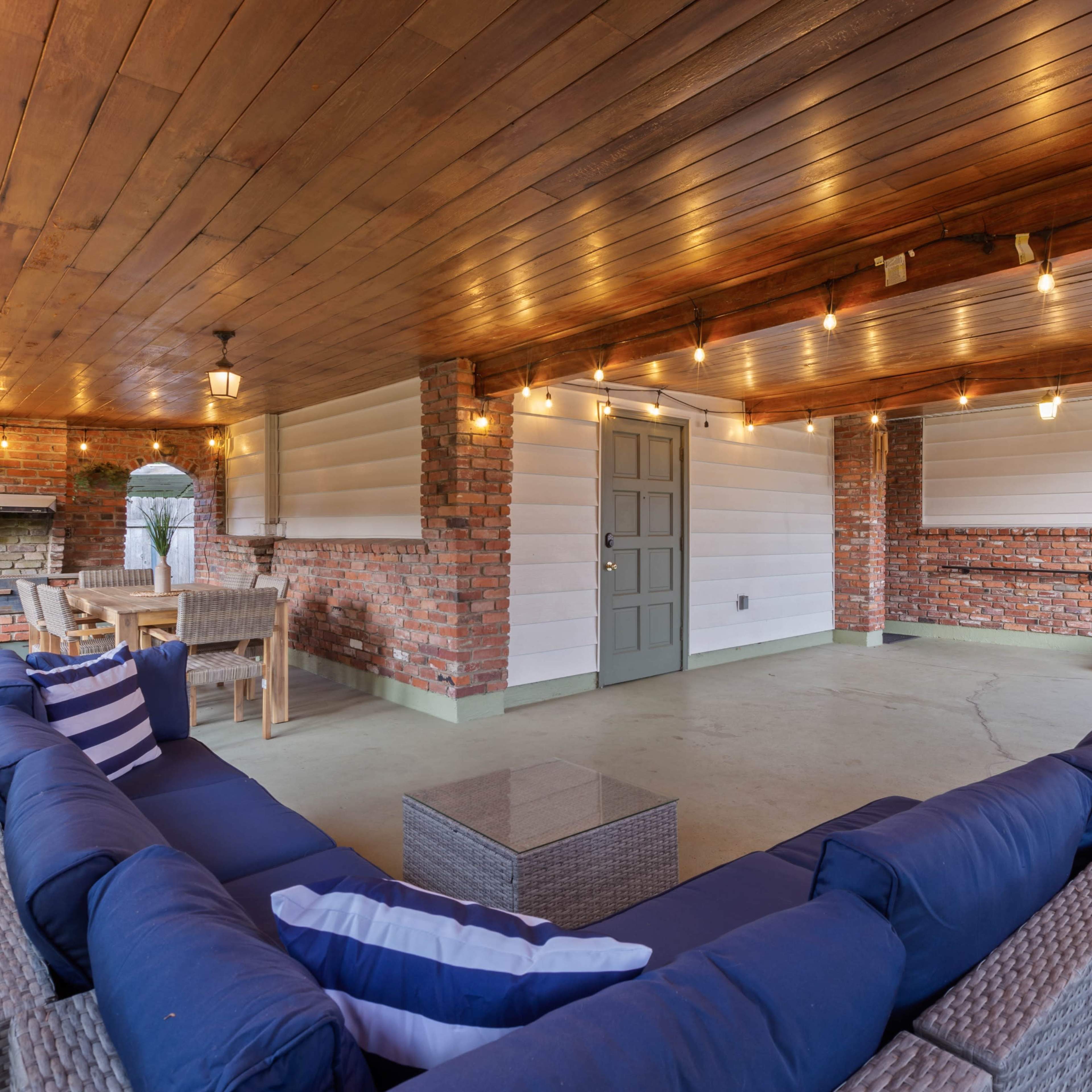 A covered outdoor patio with a seating area, dining space, and string lights overhead.