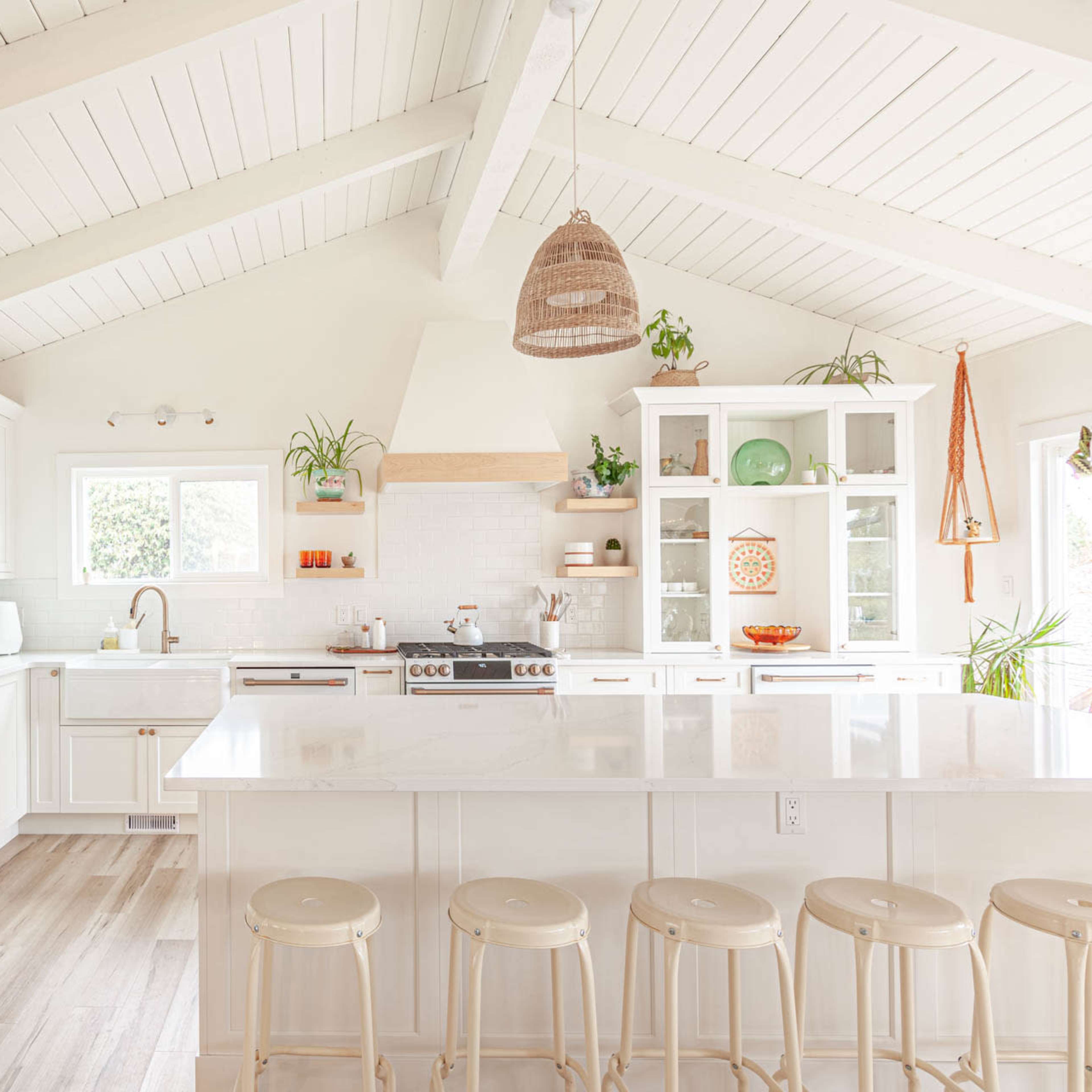 The kitchen features white cabinetry, a large island with seating, and natural light streaming in through the windows, accented by decorative plants.