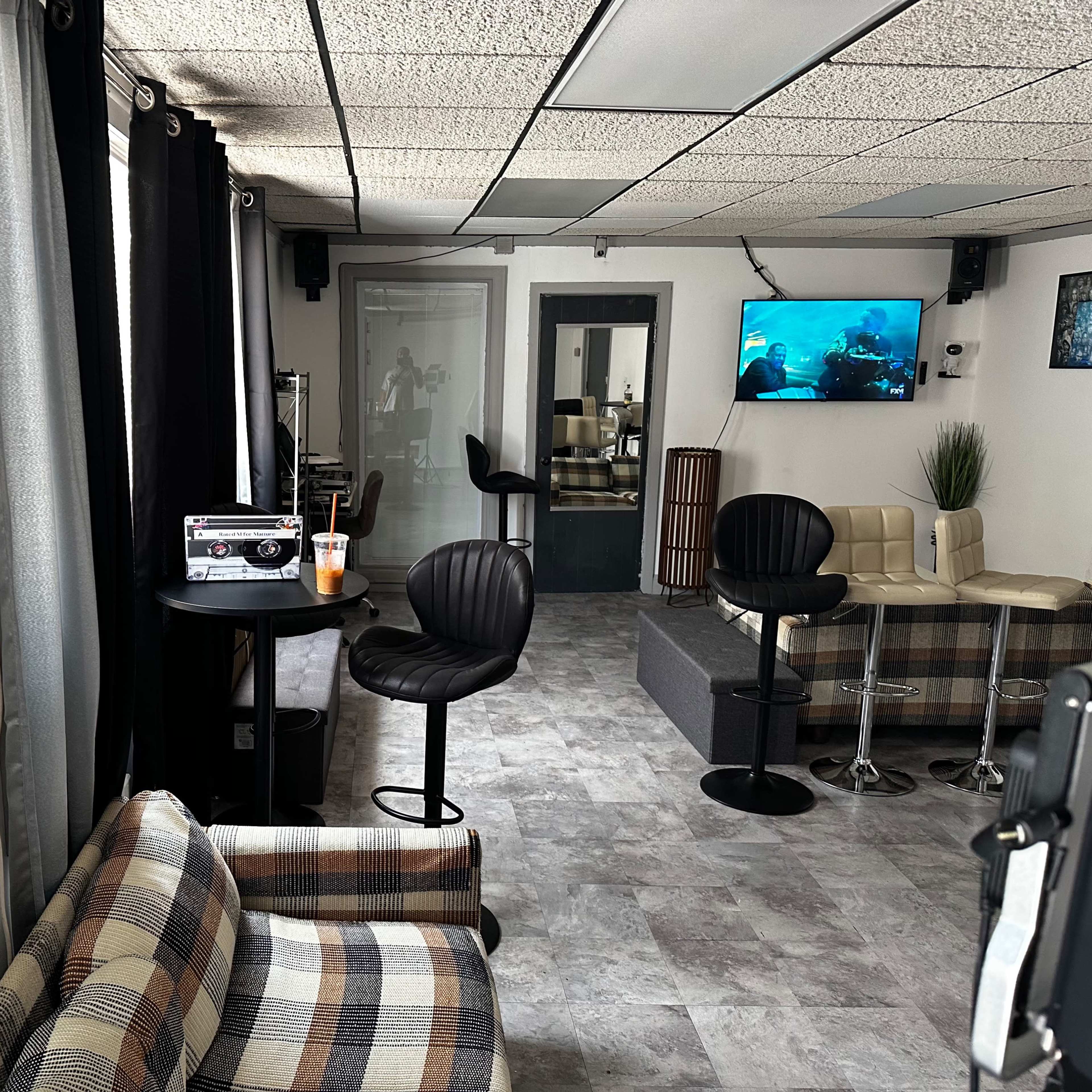 A modern lounge area with a checkered sofa, black bar stools, and two televisions mounted on the walls.