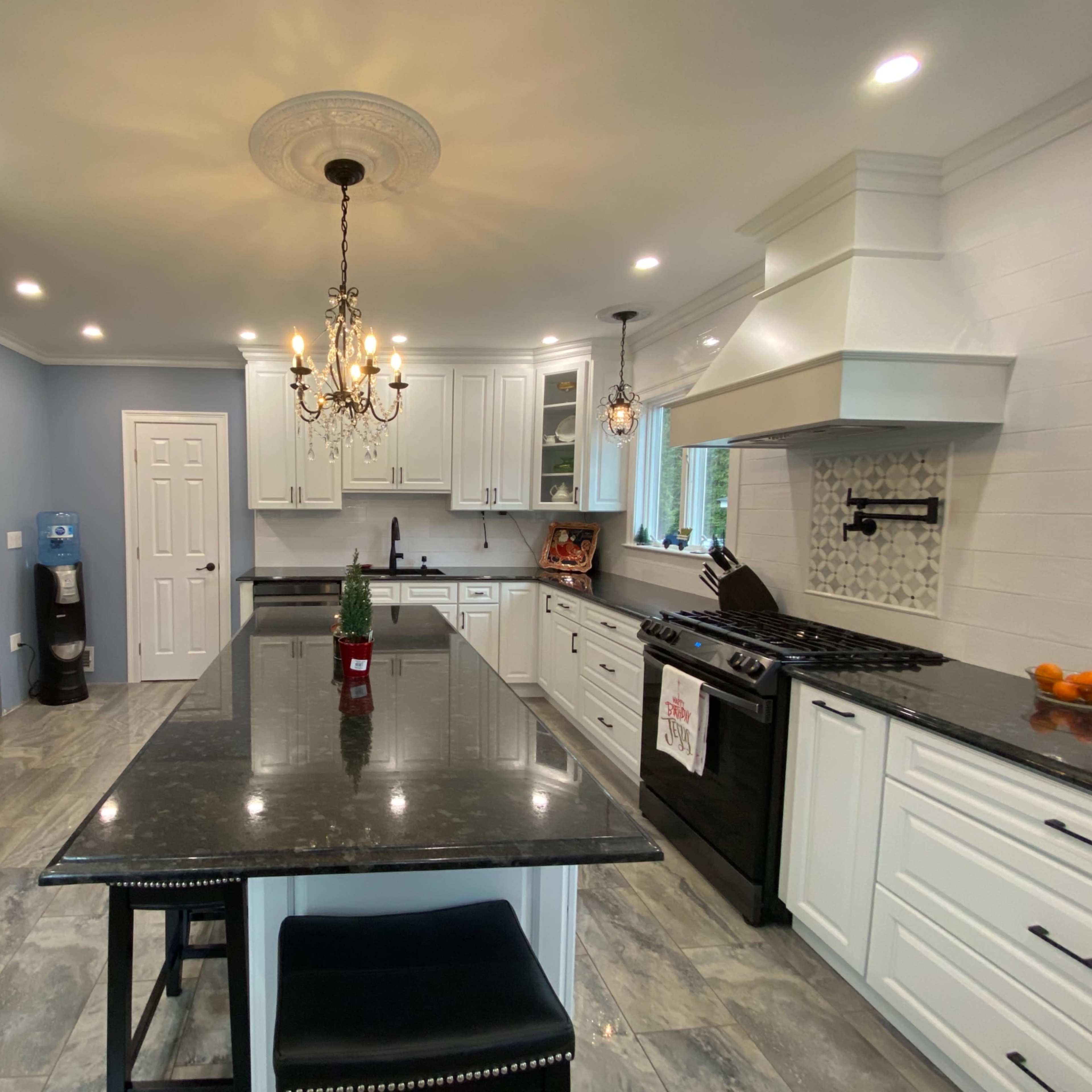 The kitchen features white cabinetry, a large black granite island, and modern appliances, including a black refrigerator and a stainless steel stove.