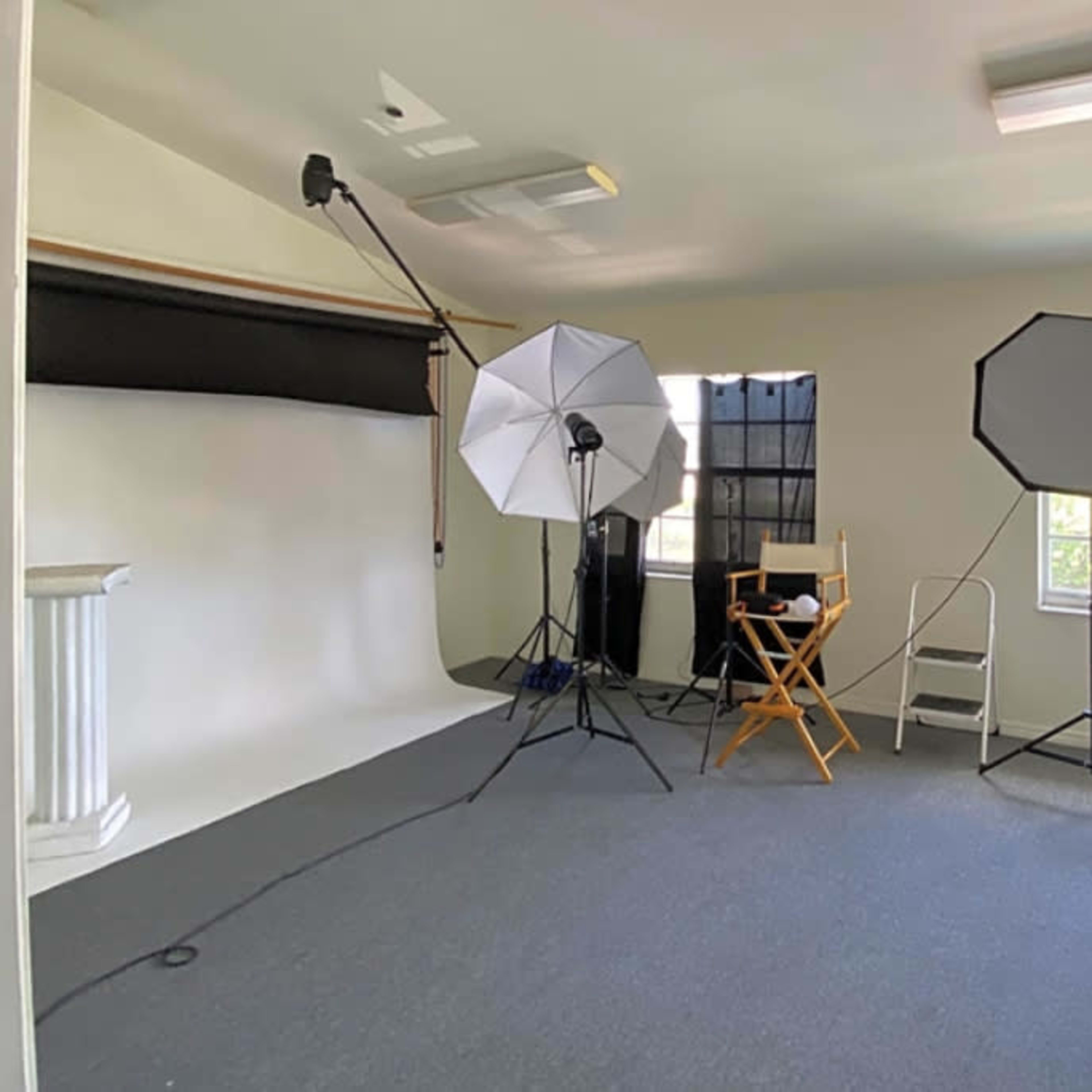 A photography studio with a backdrop, lighting equipment, and chairs arranged for a photo shoot.
