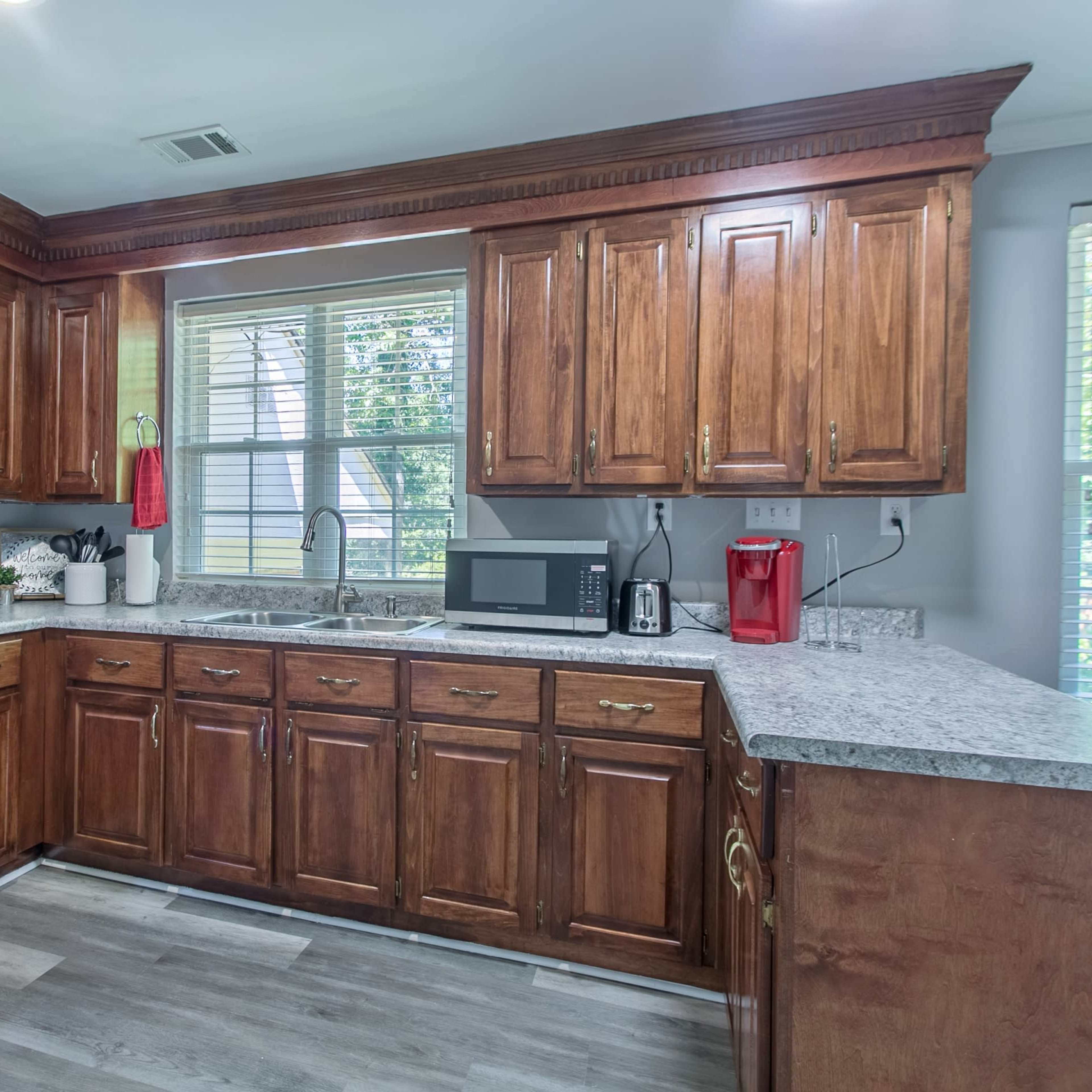A kitchen with wooden cabinets, a stainless steel oven, and a granite countertop, illuminated by natural light from a window.